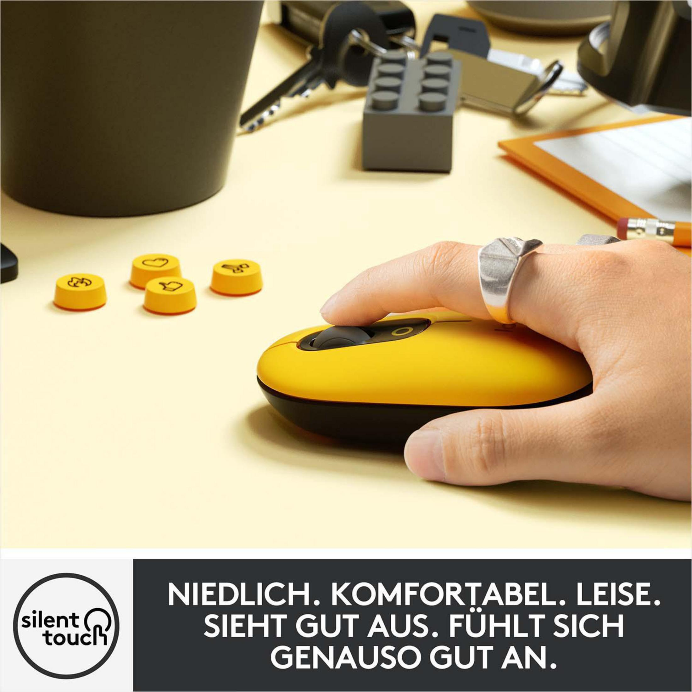 Żółto-czarna mysz Logitech, z dłonią używającą jej. Przyciski i inne przedmioty na stole.