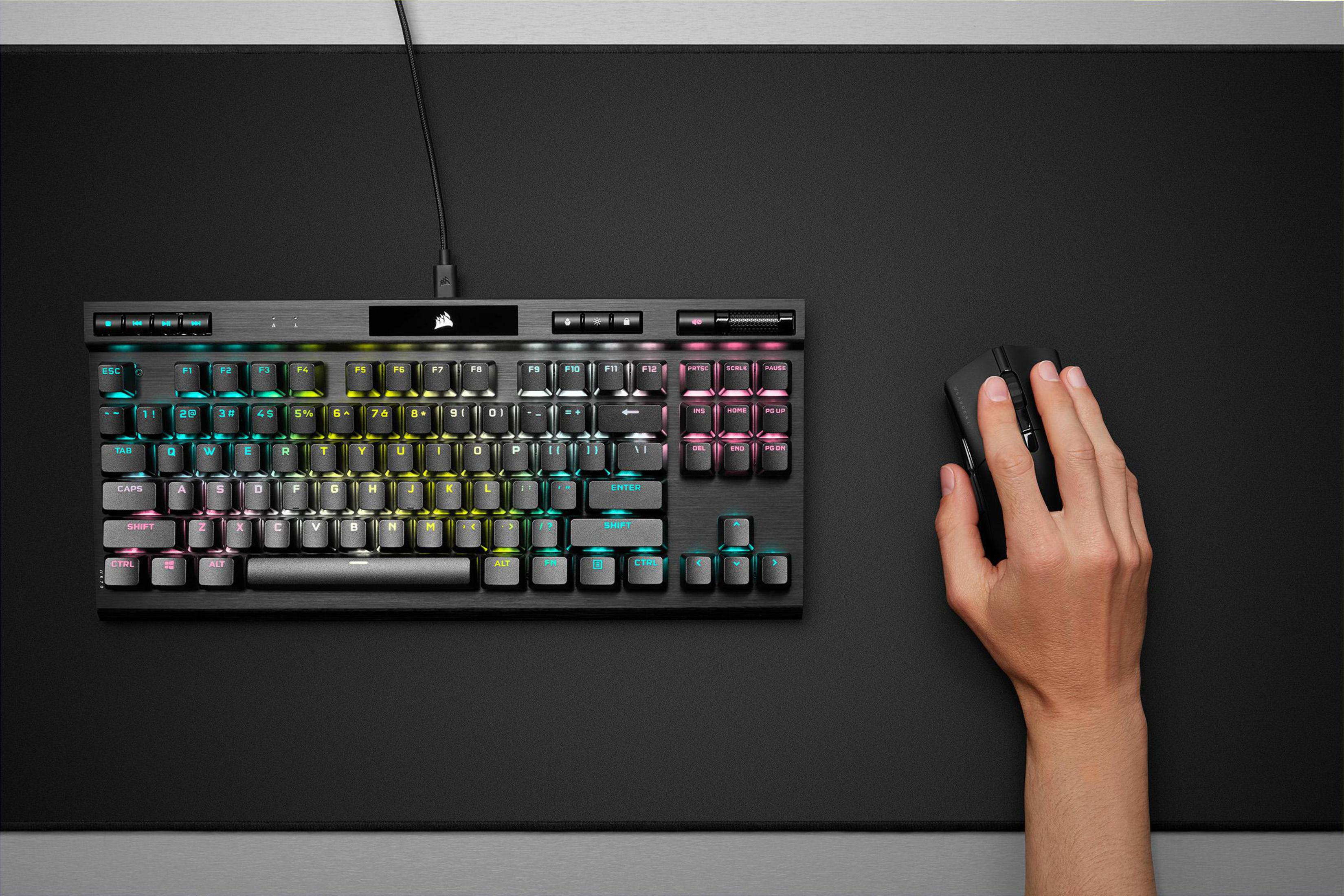 Klawiatura i mysz na czarnej podkładce. Klawiatura ma kolorowe klawisze. Ręka używa myszy.