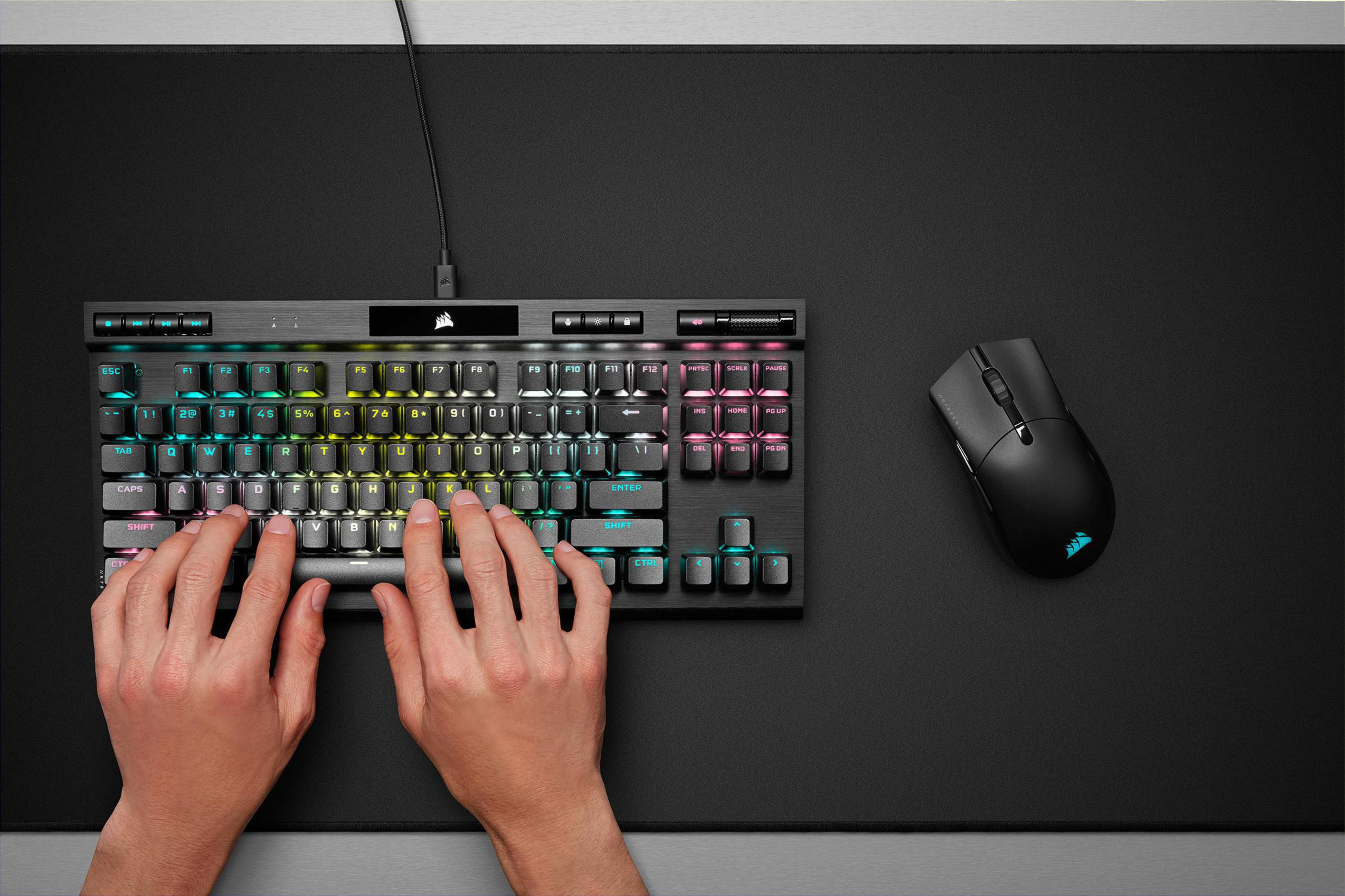 Ręce piszące na podświetlanej klawiaturze z myszą na czarnej macie.