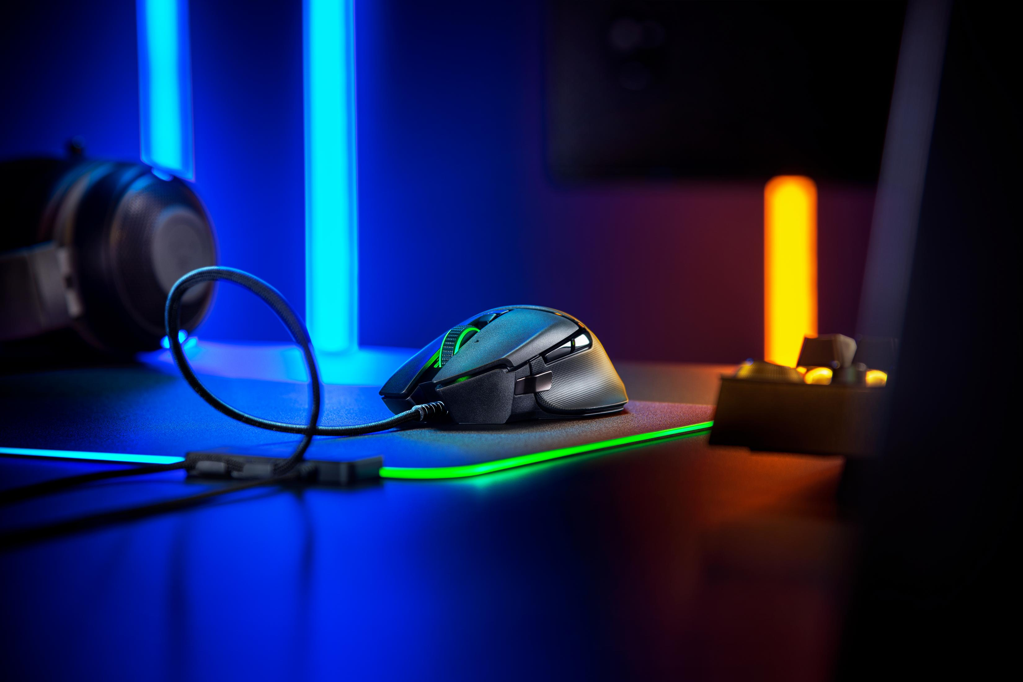 Mouse da gioco con luci verdi su un tappetino nero. Luci blu e arancioni sullo sfondo.