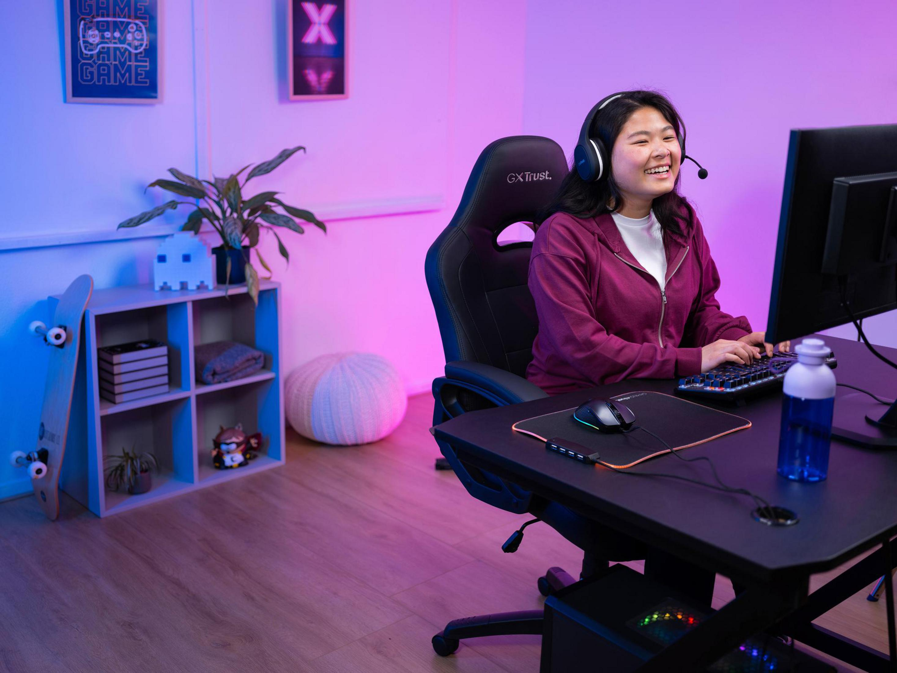 Młoda kobieta grająca, w słuchawkach, przy biurku w pokoju do gier.