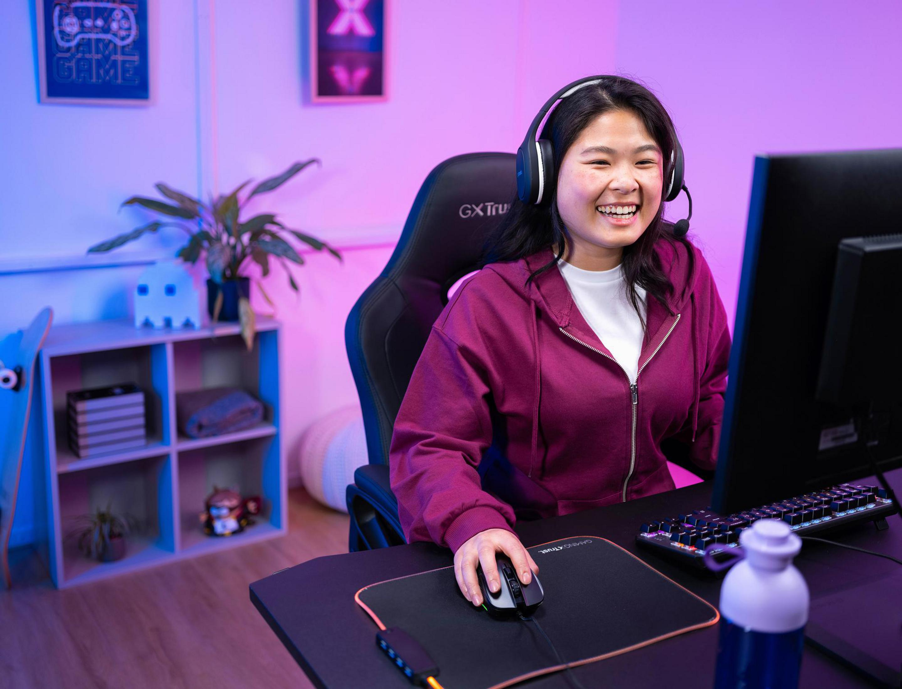 Uśmiechnięta kobieta w zestawie słuchawkowym grająca w grę na komputerze.