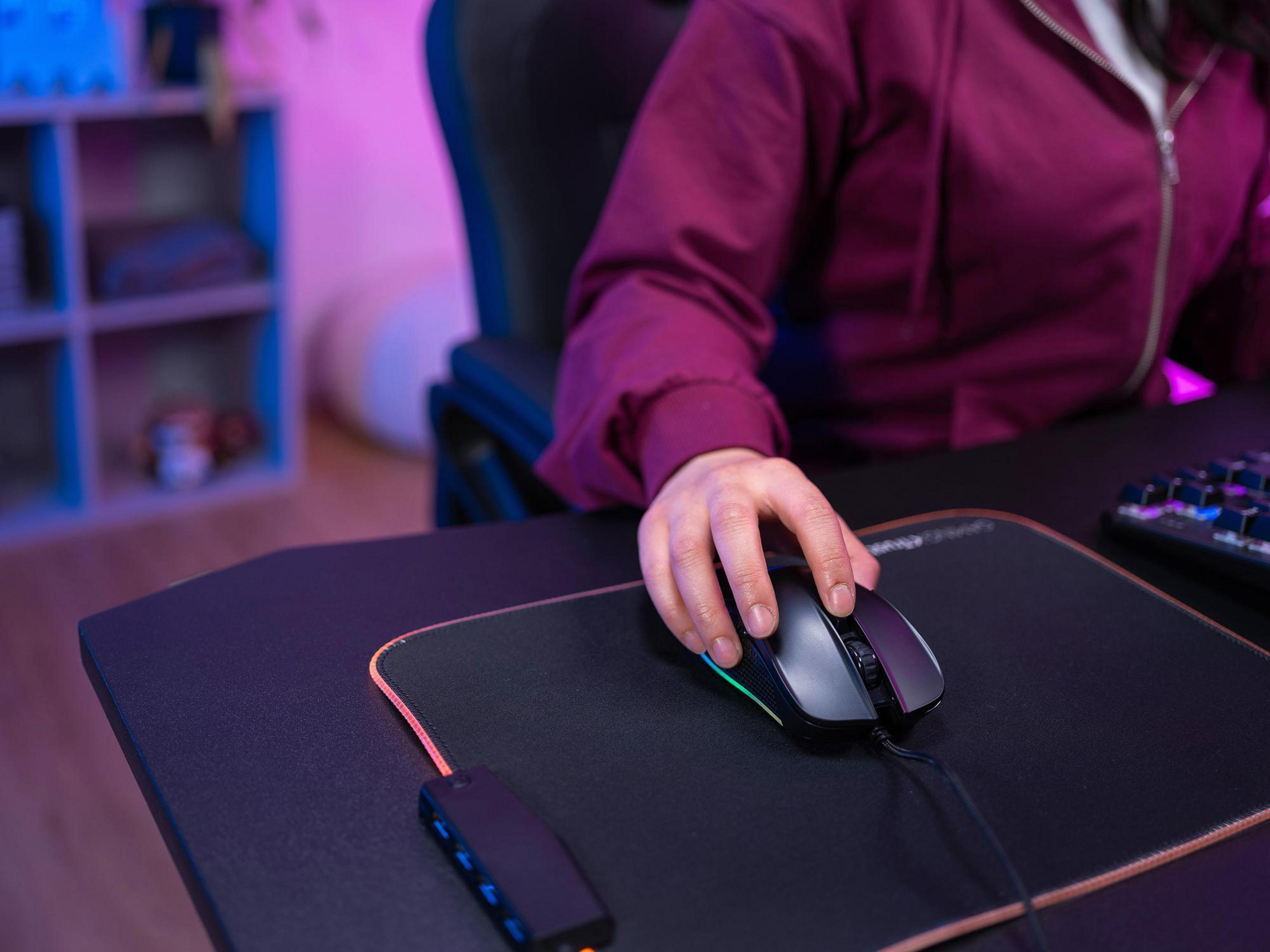 Ręka osoby używająca czarnej myszy gamingowej na podkładce na biurku.