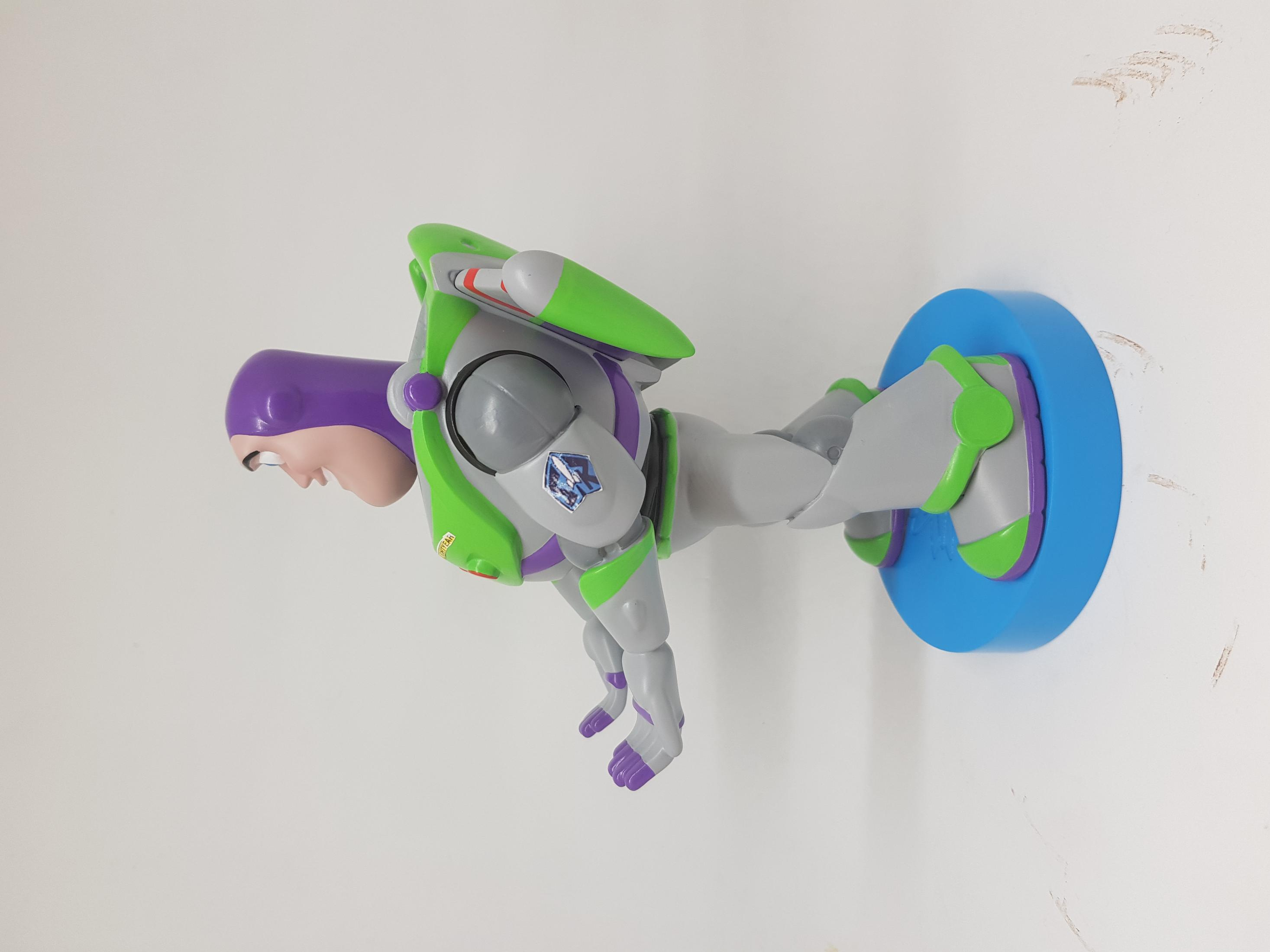 Giocattolo di Buzz Lightyear con design verde e viola, a mezz'aria da una base blu, sfondo parete bianca.