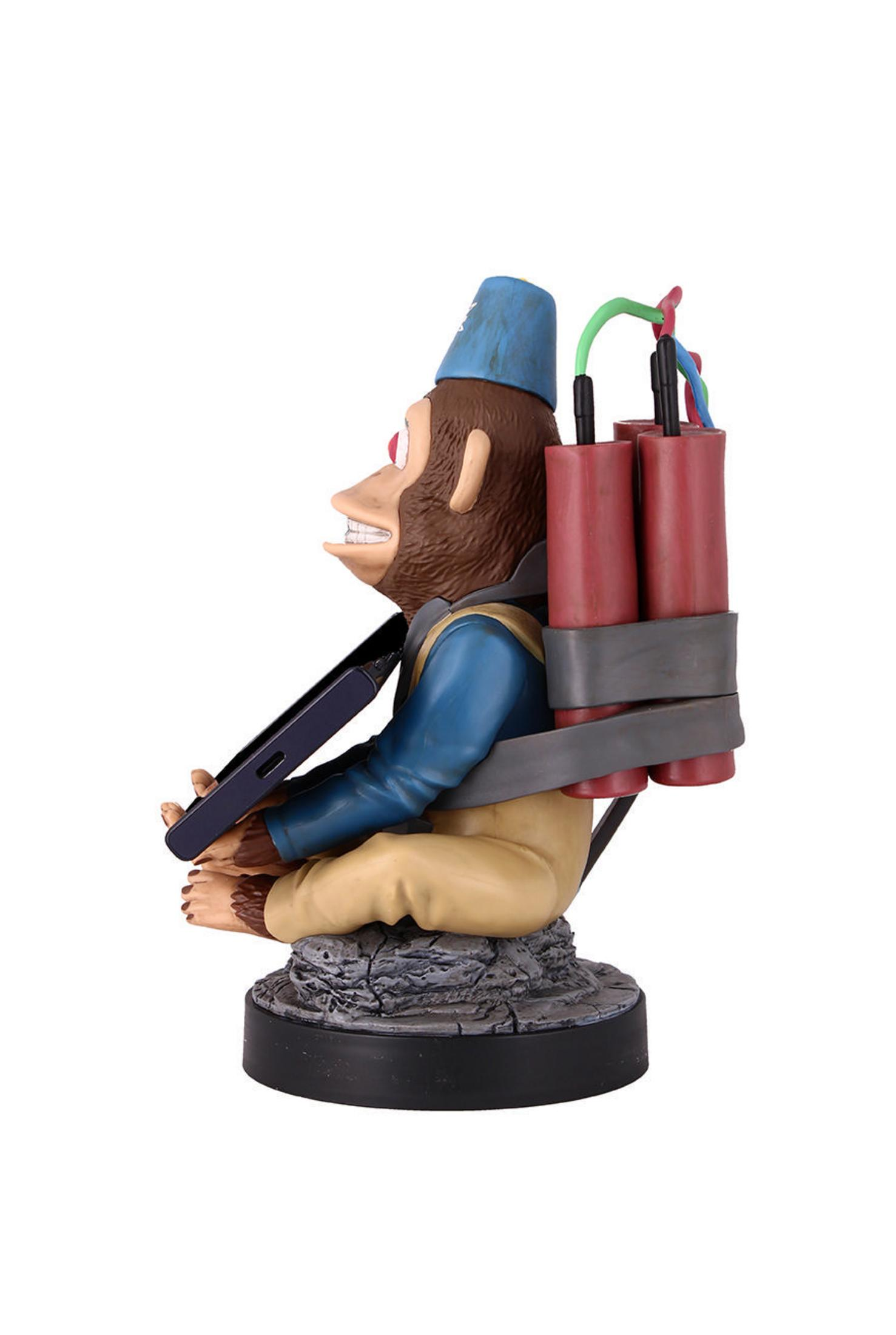 Affenfigur mit Dynamit, blauer Hut, sitzend, Telefon haltend, auf felsiger Basis, weißer Hintergrund.