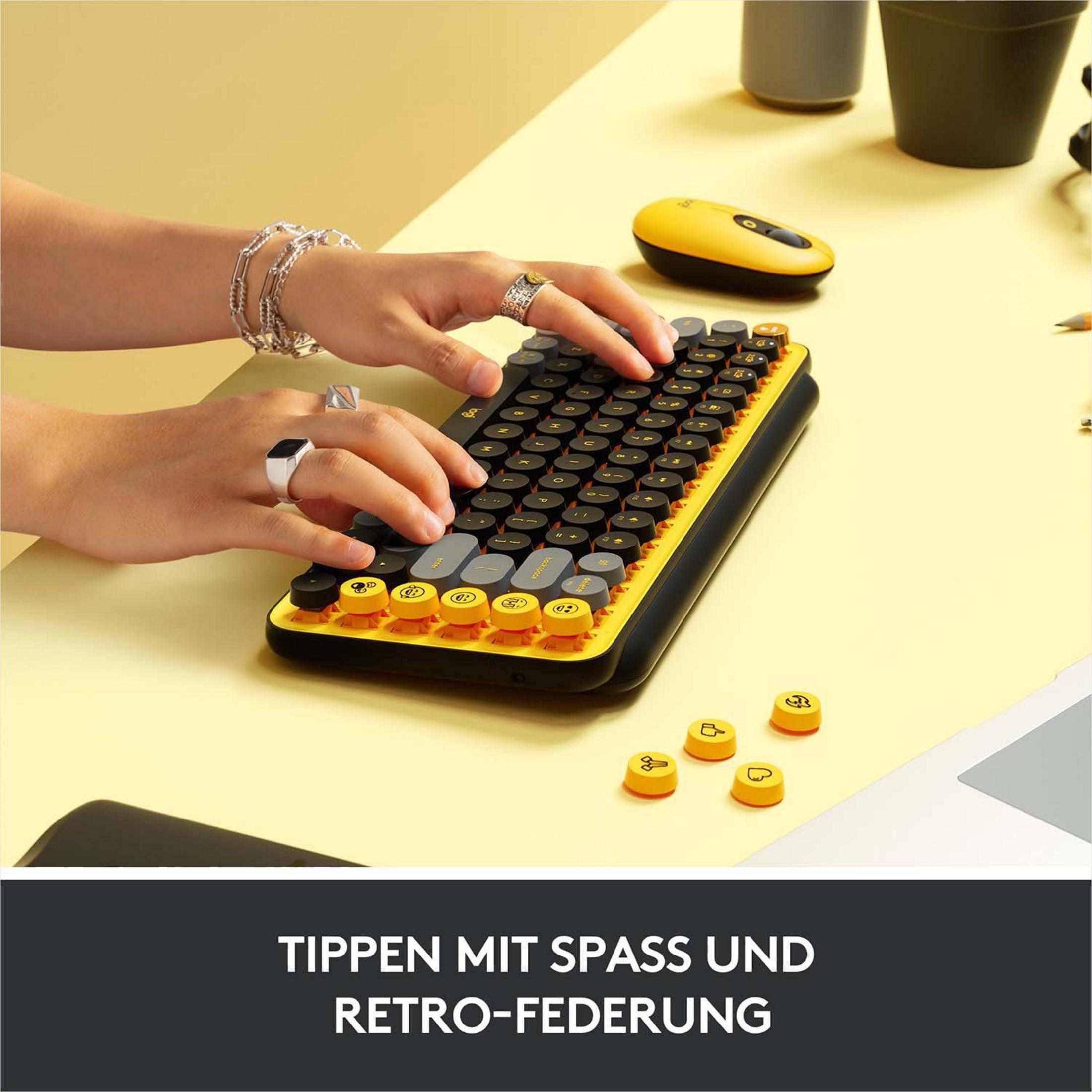 Hände, die auf einer gelb-schwarzen Tastatur tippen. Gelber Schreibtisch, mit anderen Gegenständen.