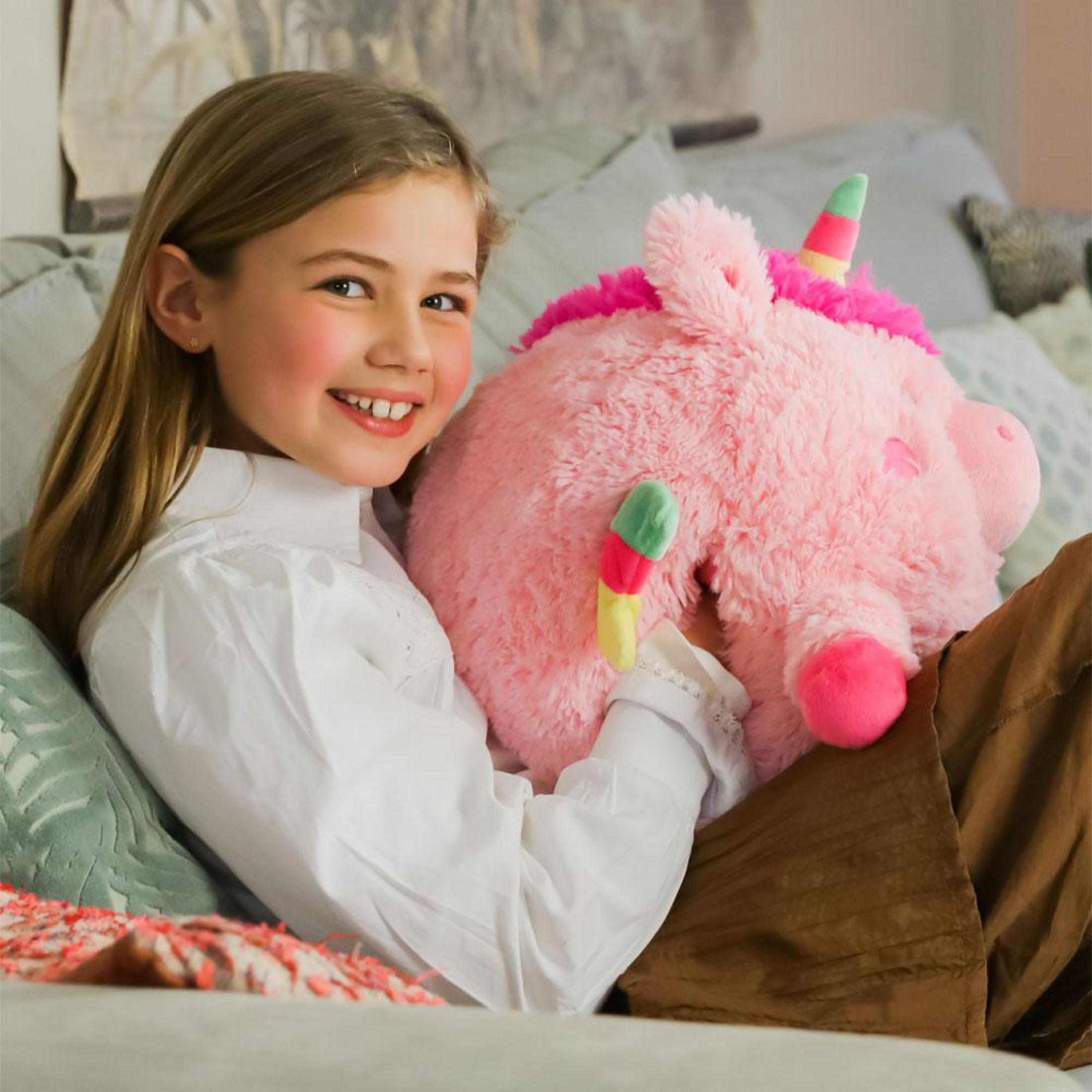 Ein Mädchen lächelt und hält ein rosa Einhorn-Plüschtier auf einem Sofa.