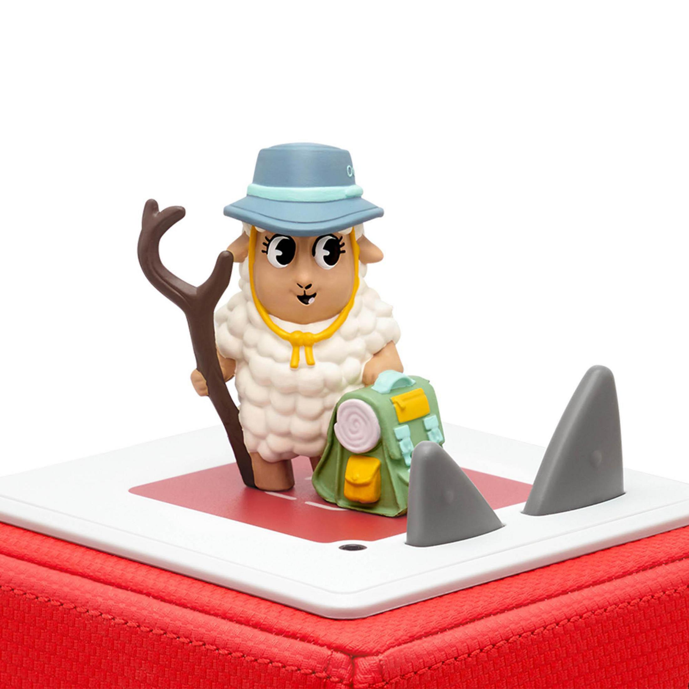 Eine Schaf-Figur mit blauem Hut, steht in der Nähe von Haifischflossen und einem grünen Rucksack. Rote Boxbasis.