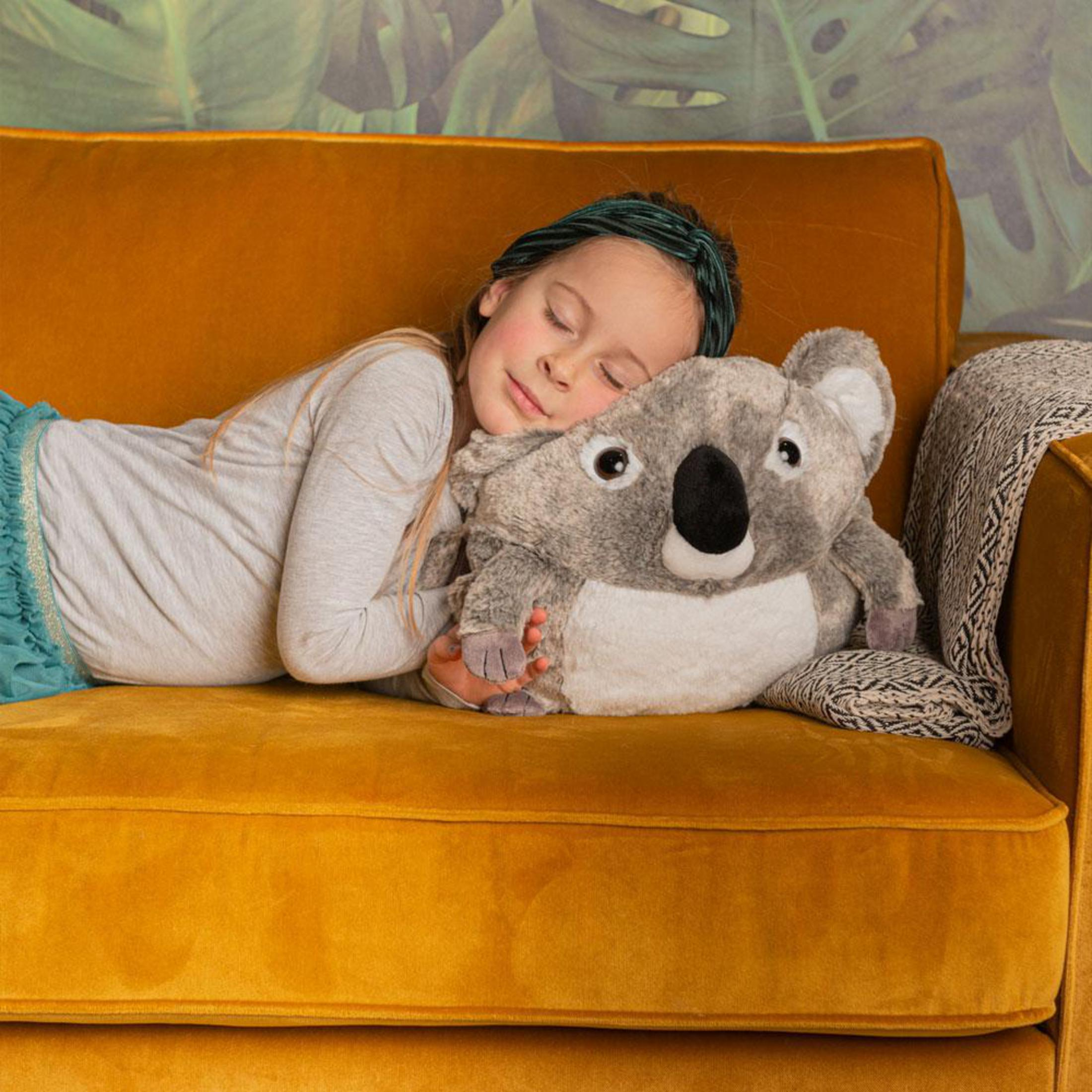 Ein Mädchen schläft auf einem gelben Sofa und umarmt ein Koala-Plüschtier.