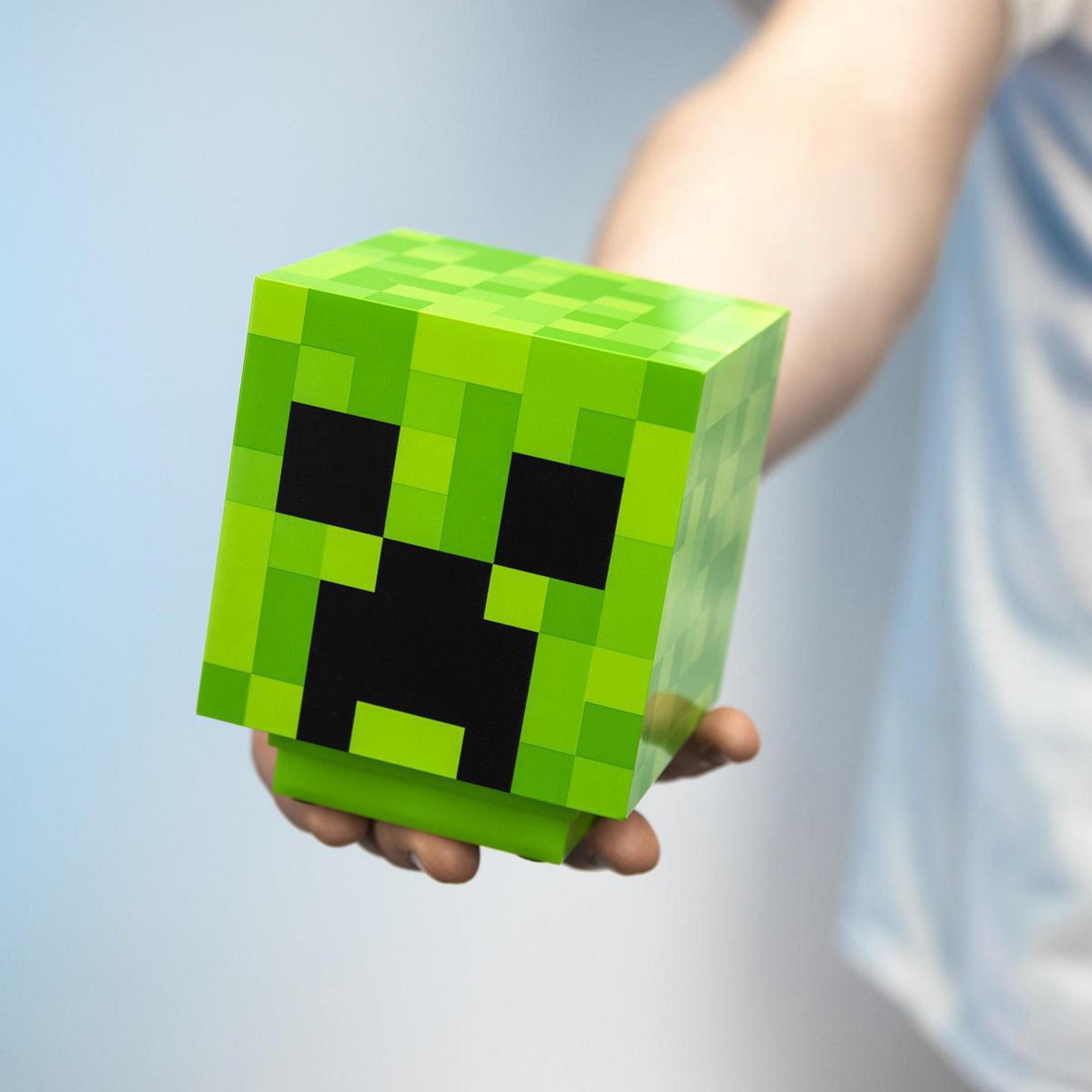 Głowa Creepera z Minecraft, trzymana w dłoni. Głowa jest zielona, pikselowana i ma czarną twarz.