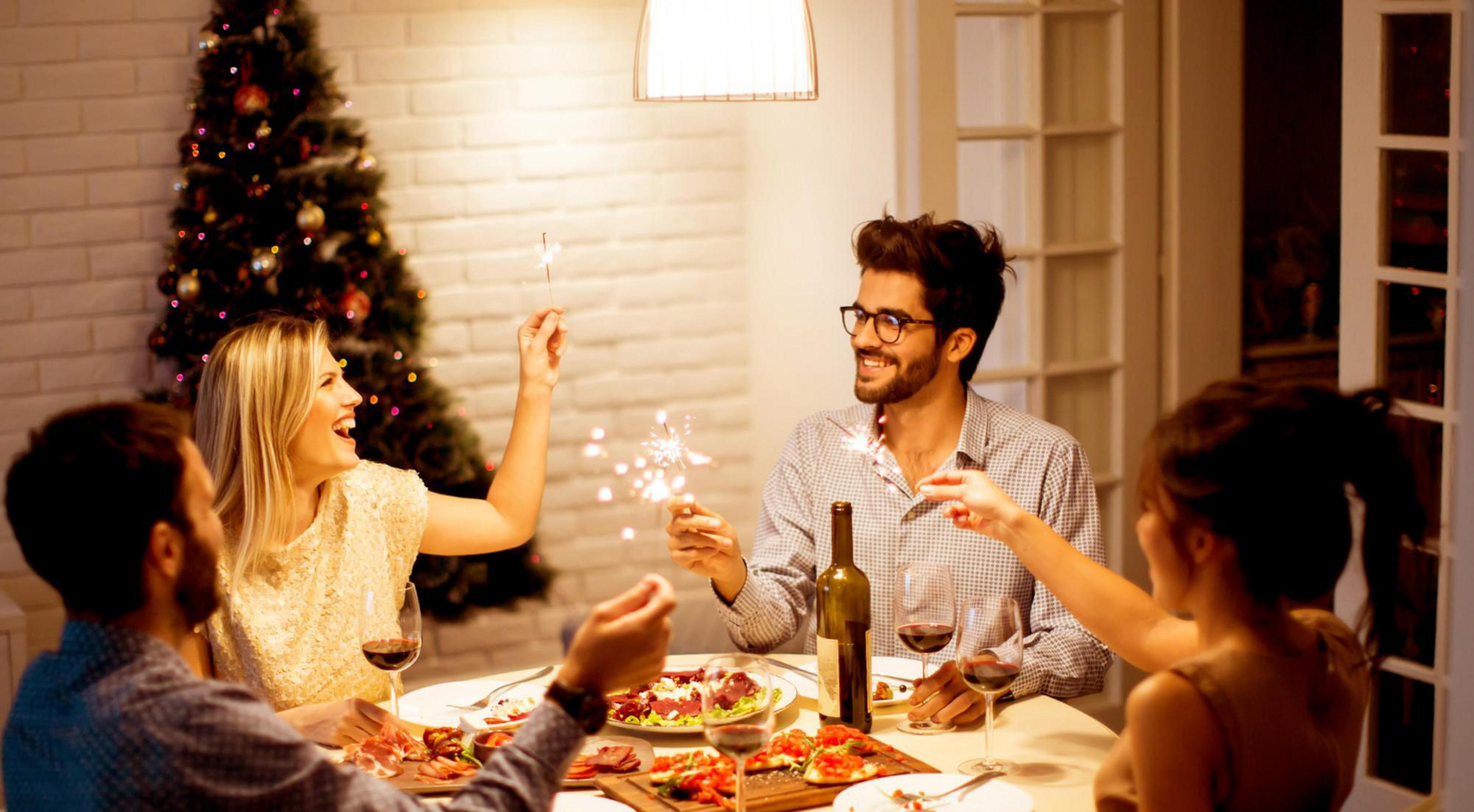 Grupa przyjaciół świętuje przy stole. Trzymają zimne ognie i butelkę wina.