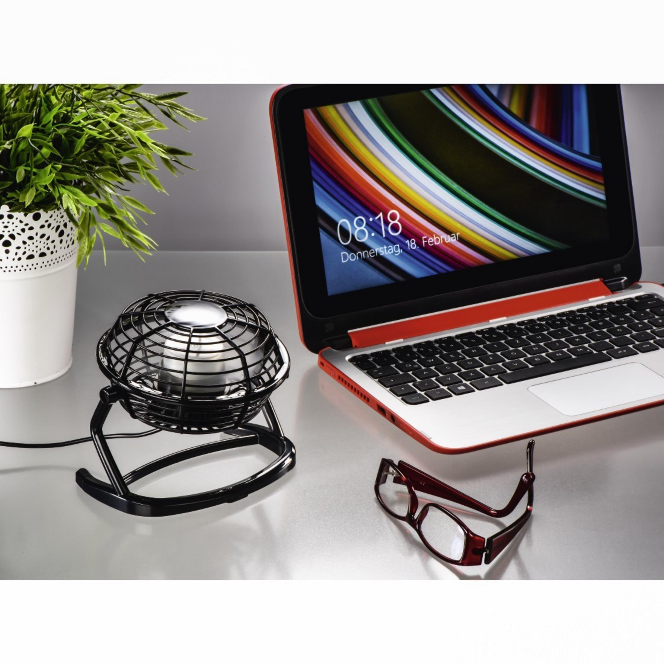 Ein kleiner schwarzer Ventilator, ein Laptop und eine Brille auf einem Tisch.
