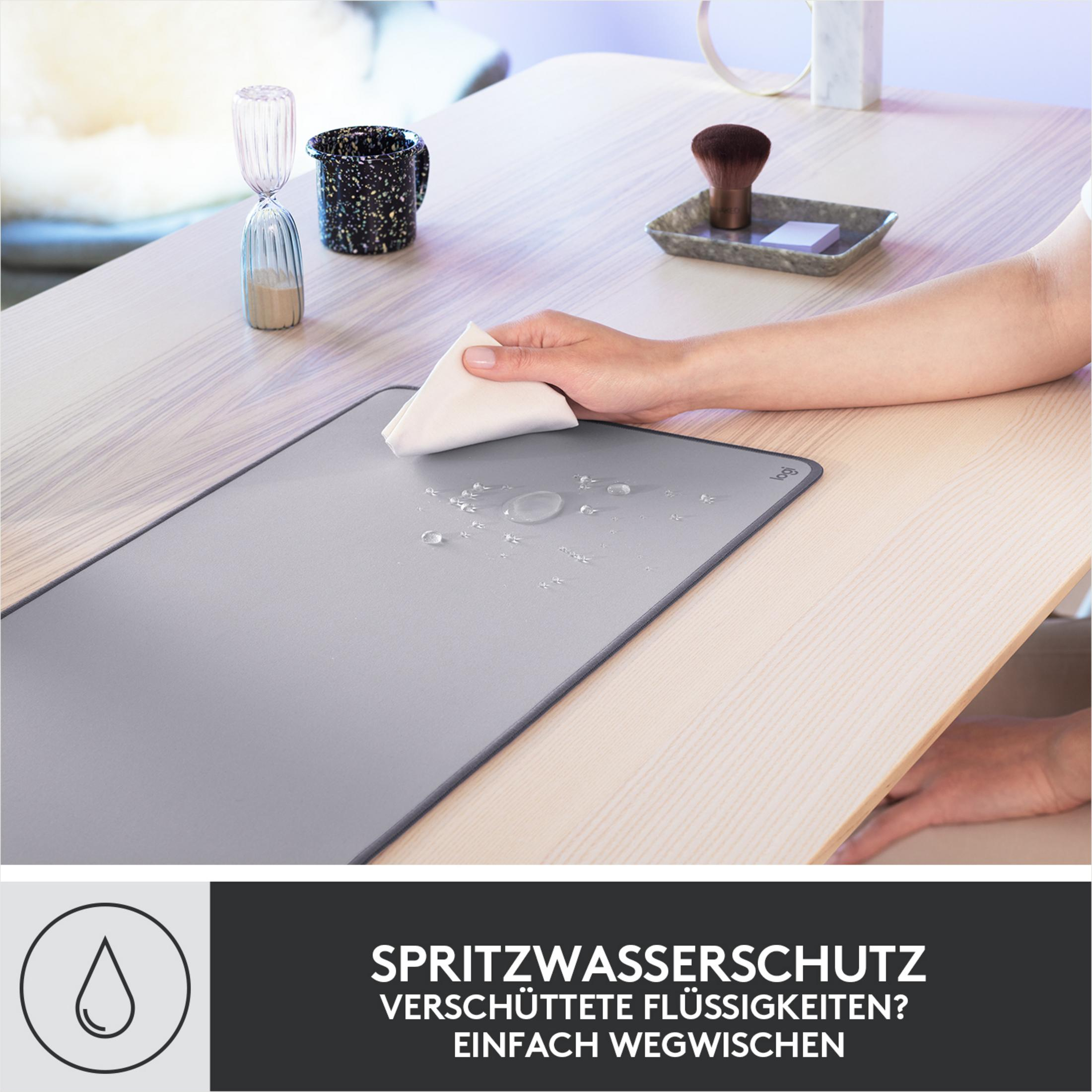 Szara podkładka pod mysz z kroplami wody i dłonią wycierającą ją, jasne drewniane tło.