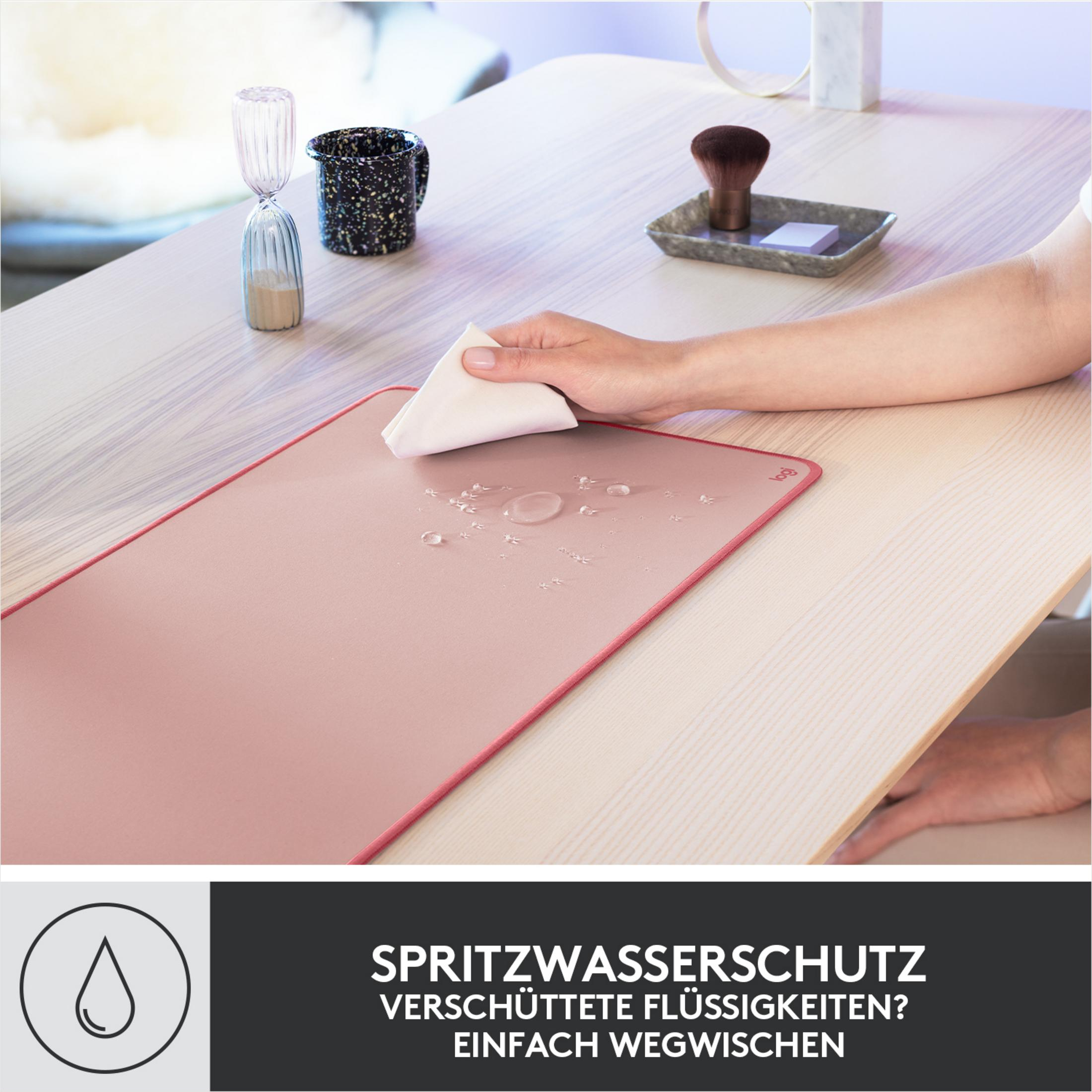 Ręka wyciera krople wody z różowej podkładki pod mysz.