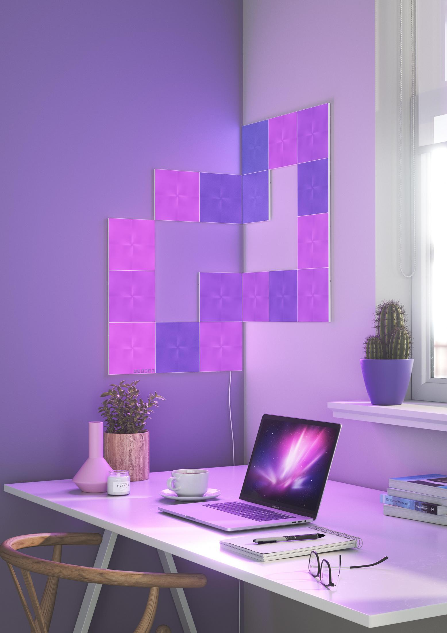 Decorazioni murali viola con luci, scrivania con laptop e accessori. Un cactus e un vaso sono visibili.