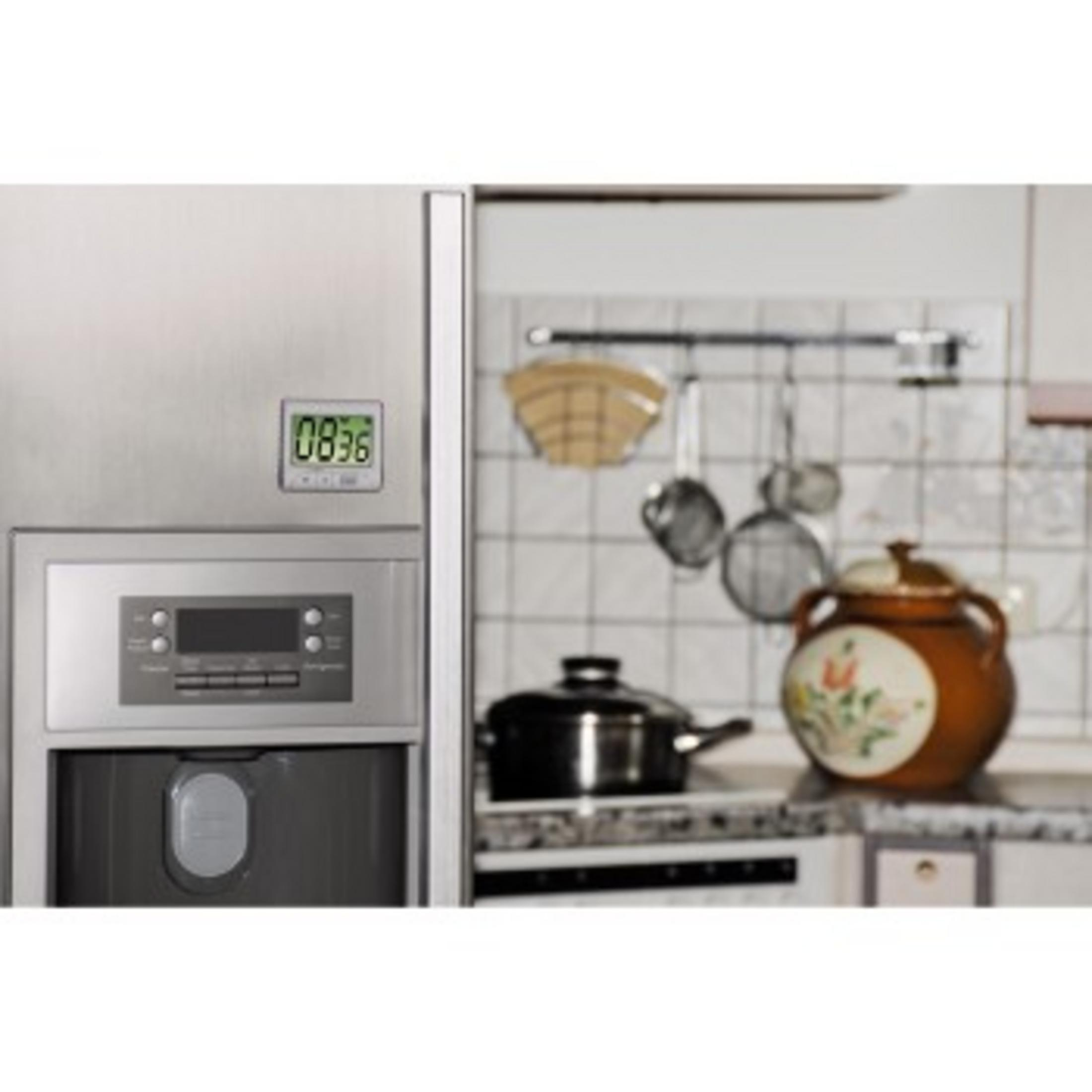 Ein Edelstahlkühlschrank mit Digitaluhr und eine Küchenszene im Hintergrund.