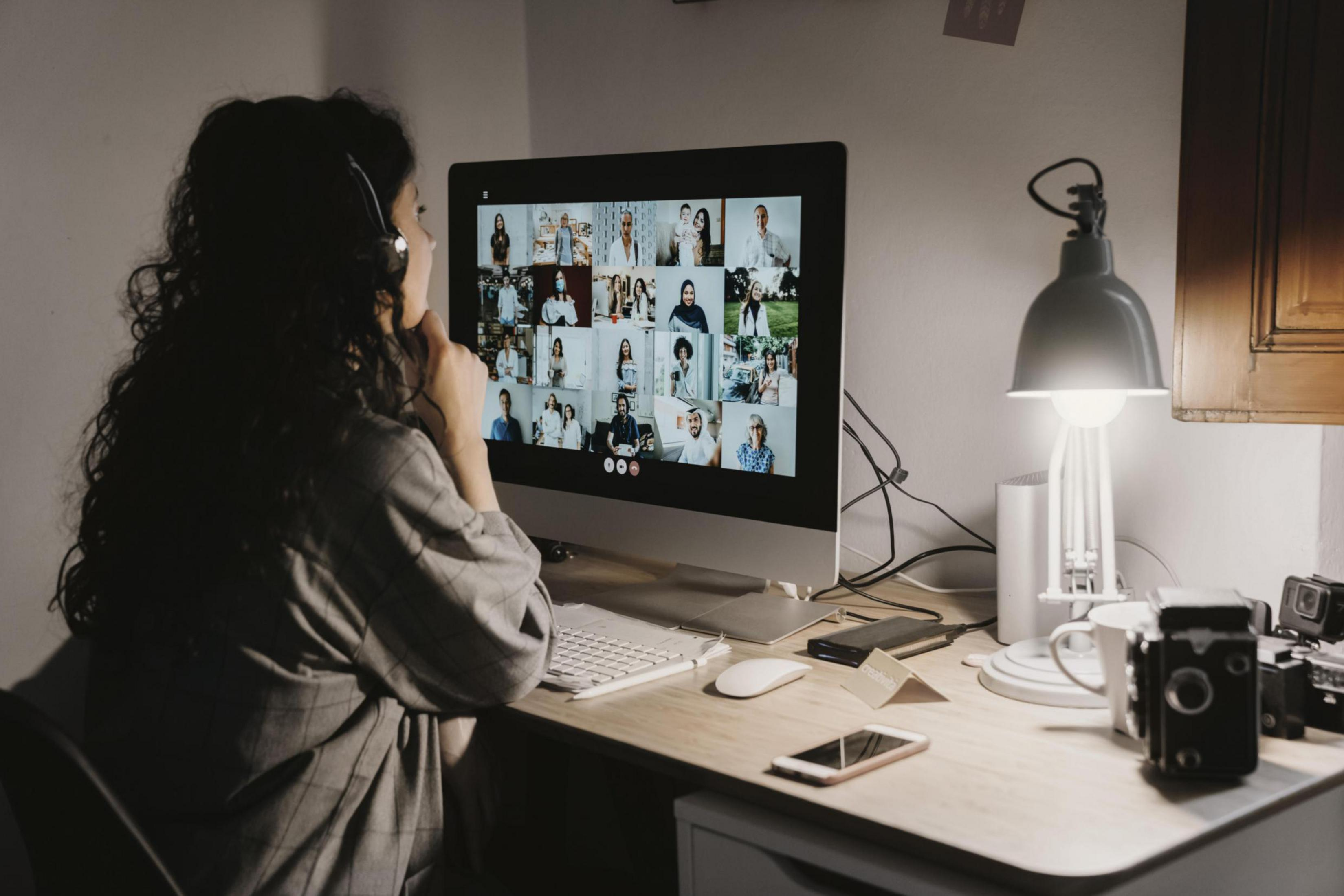 Una donna in videochiamata con molti partecipanti sullo schermo di un computer, che lavora a una scrivania.