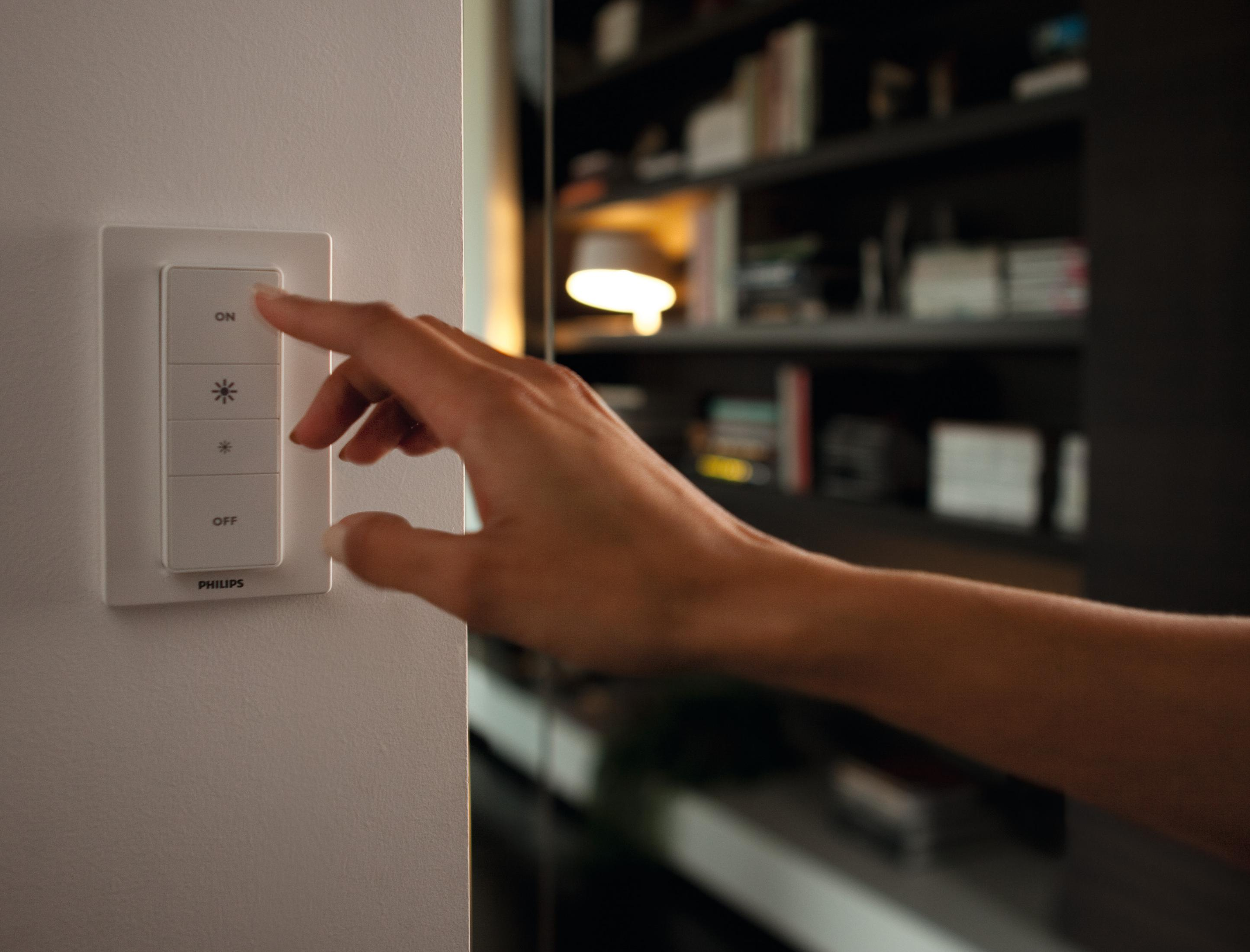 Die Hand einer Person drückt einen Philips Smart-Lichtschalter an einer weißen Wand.