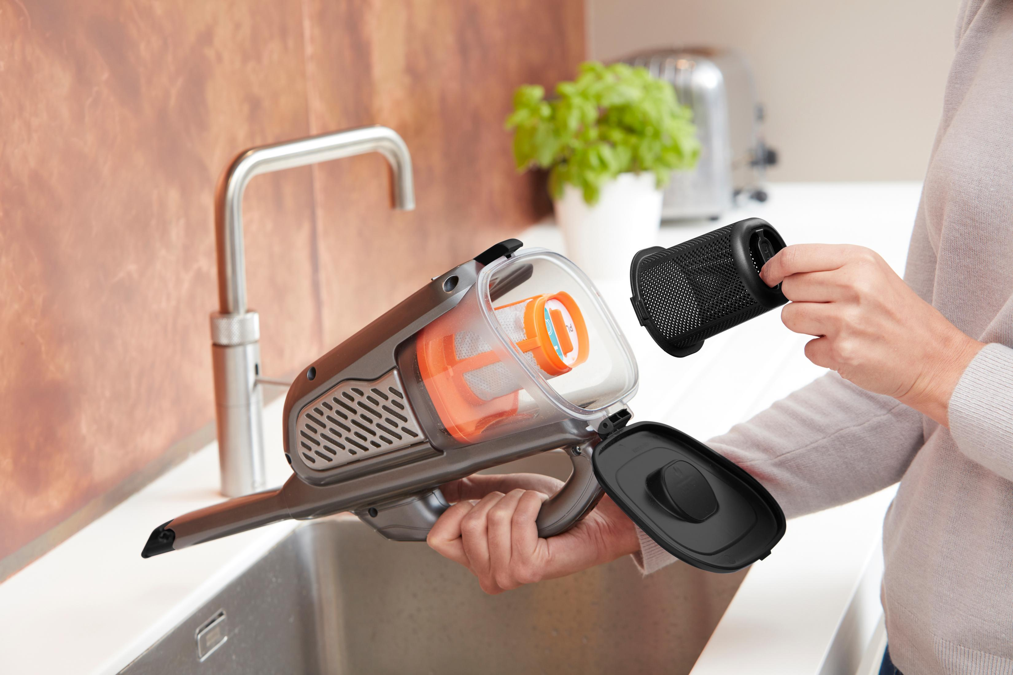 A woman holding a vacuum cleaner, removing a filter near a sink.