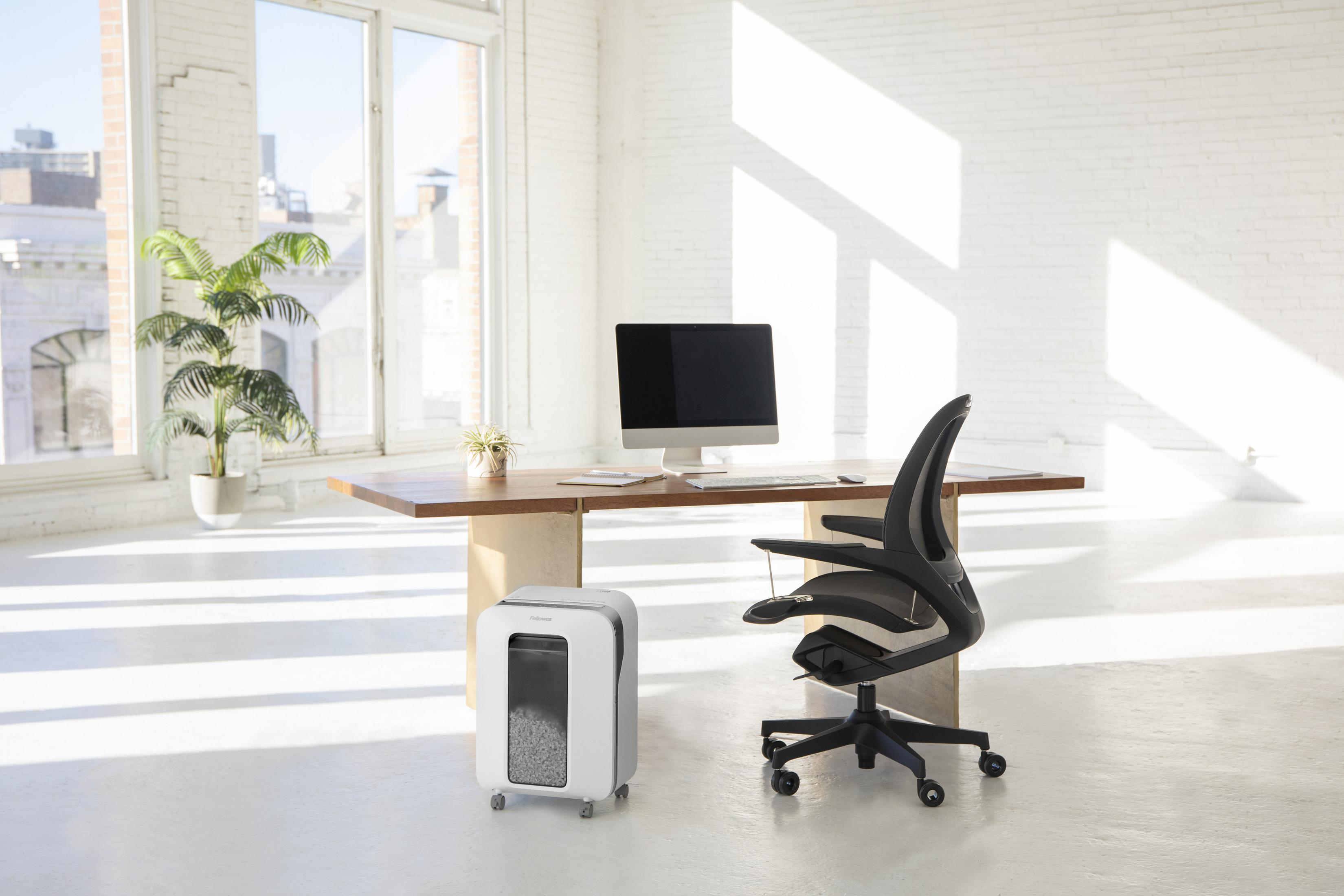 Biuro z biurkiem, komputerem, krzesłem i niszczarką do papieru.