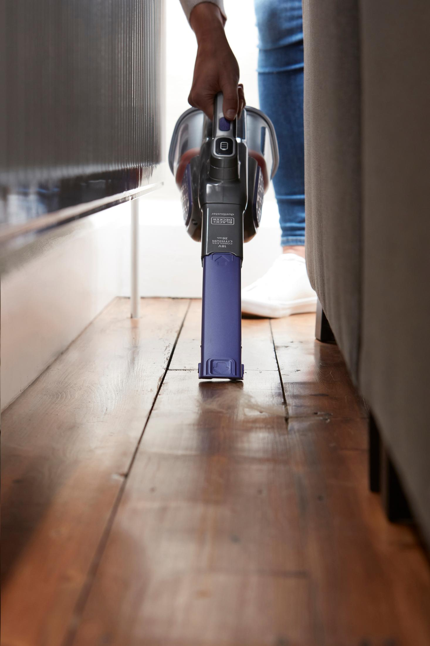 Osoba używa czarno-fioletowego odkurzacza do czyszczenia drewnianej podłogi w pokoju.