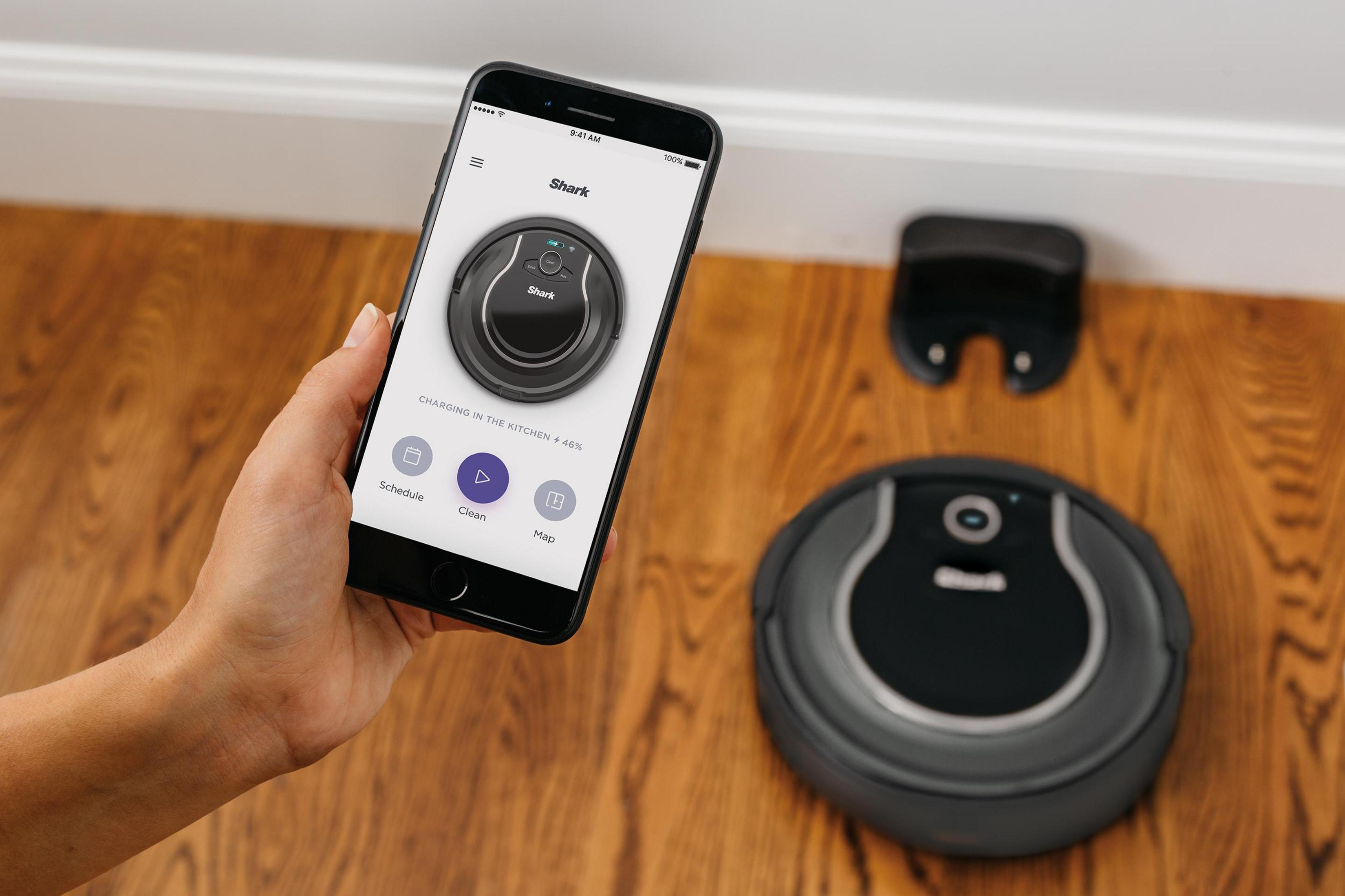 Persona sosteniendo teléfono mostrando la app. Aspiradora robot y base.