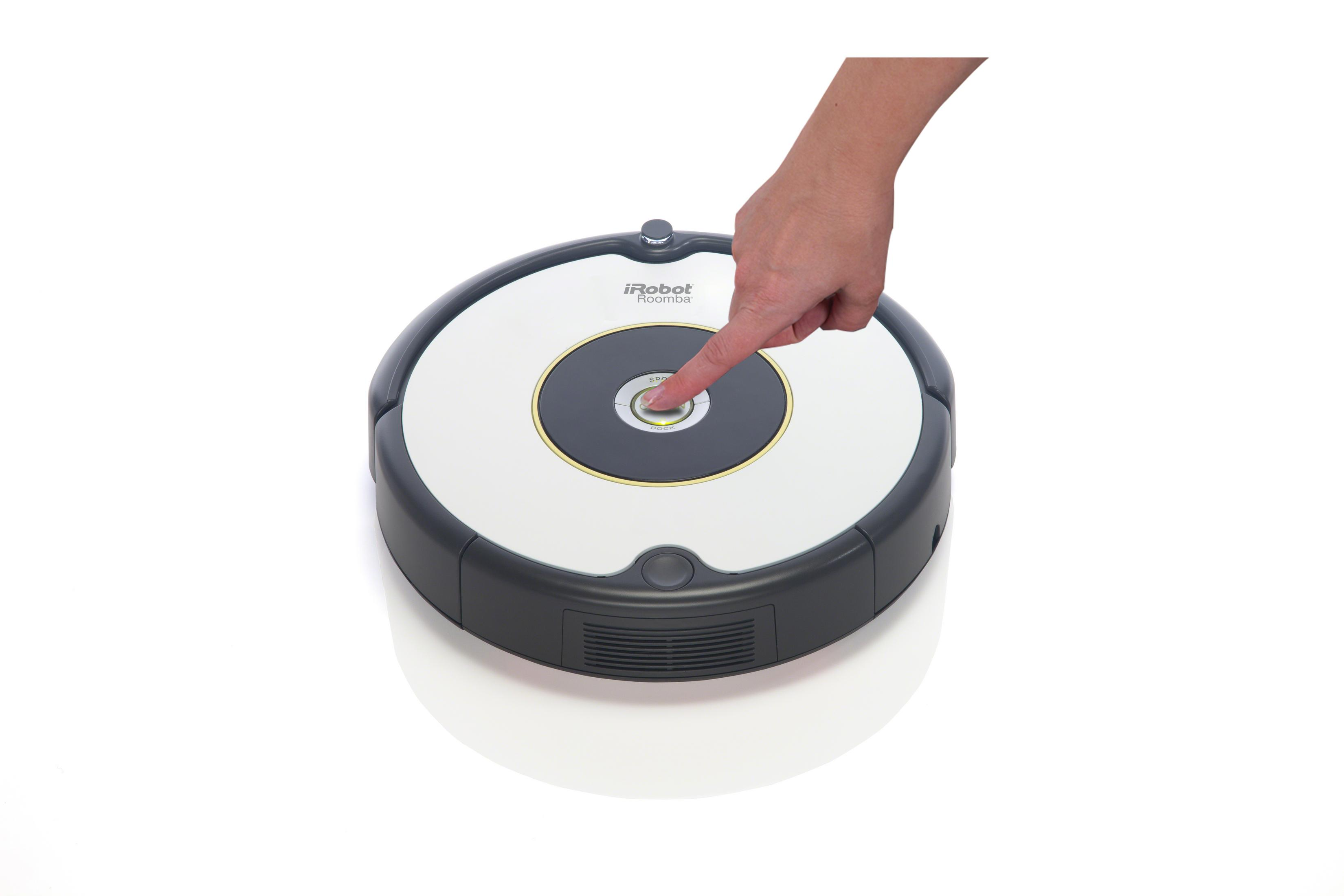 Ręka naciskająca przycisk start na białym i czarnym odkurzaczu Roomba.