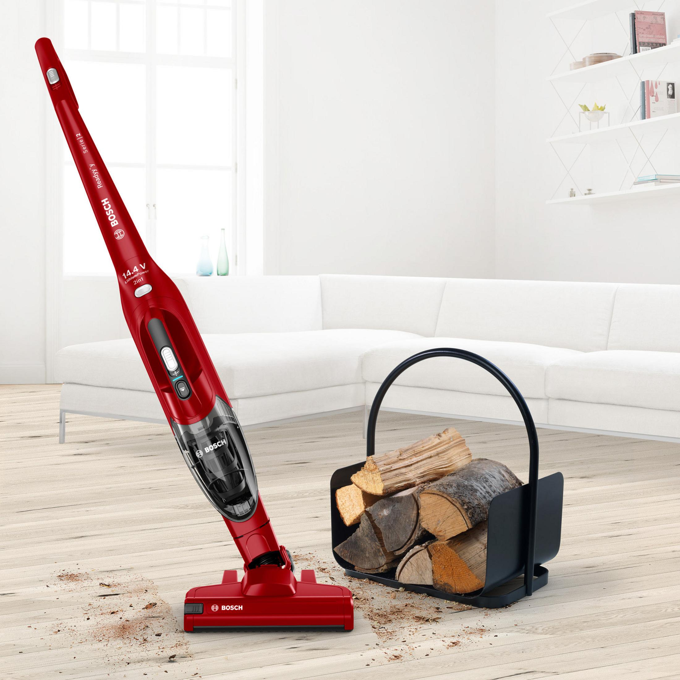 Czerwony odkurzacz bezprzewodowy obok czarnego kosza na drewno na drewnianej podłodze.