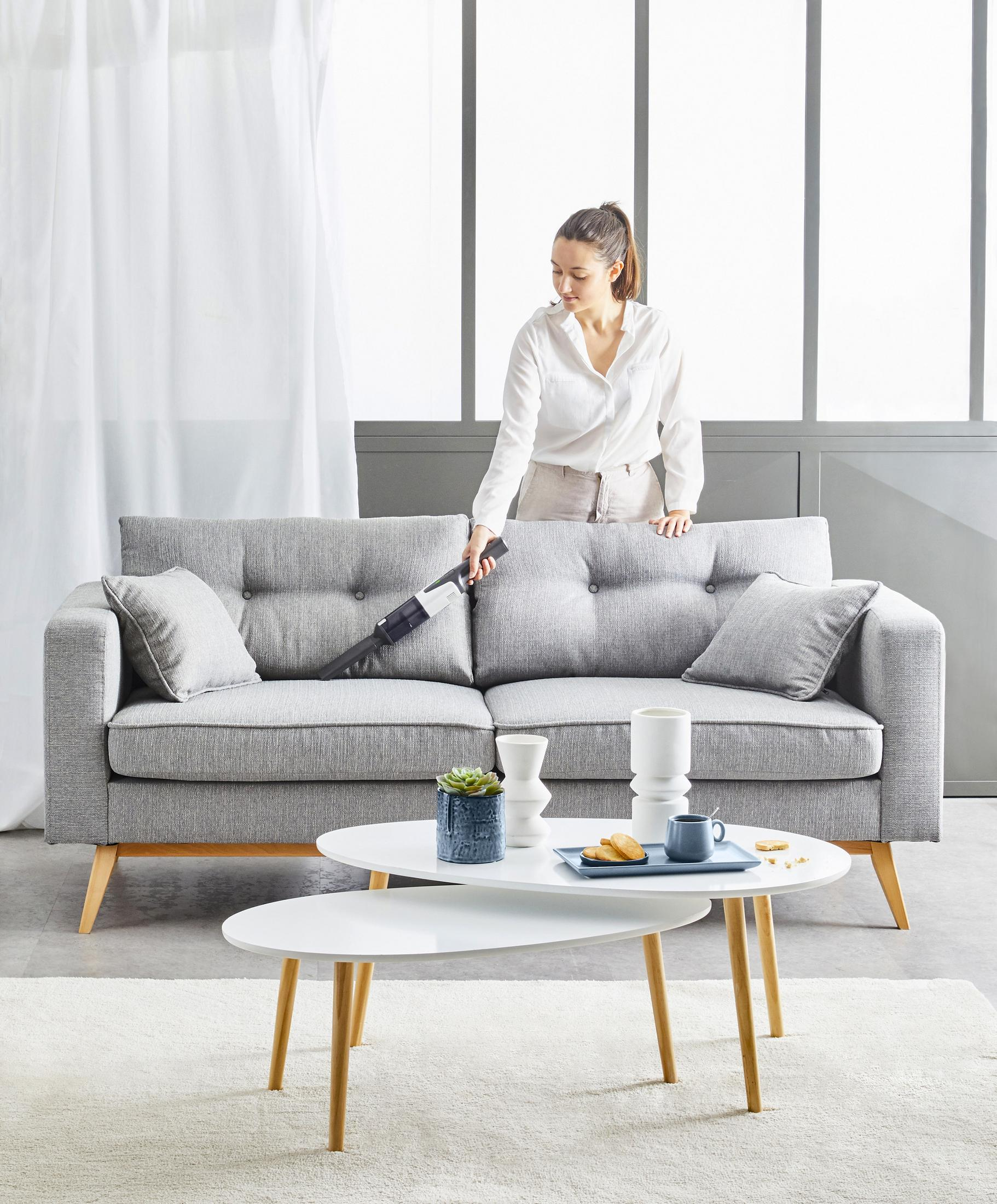 Vrouw die een bank stofzuigt, met salontafel en decoratieve items.
