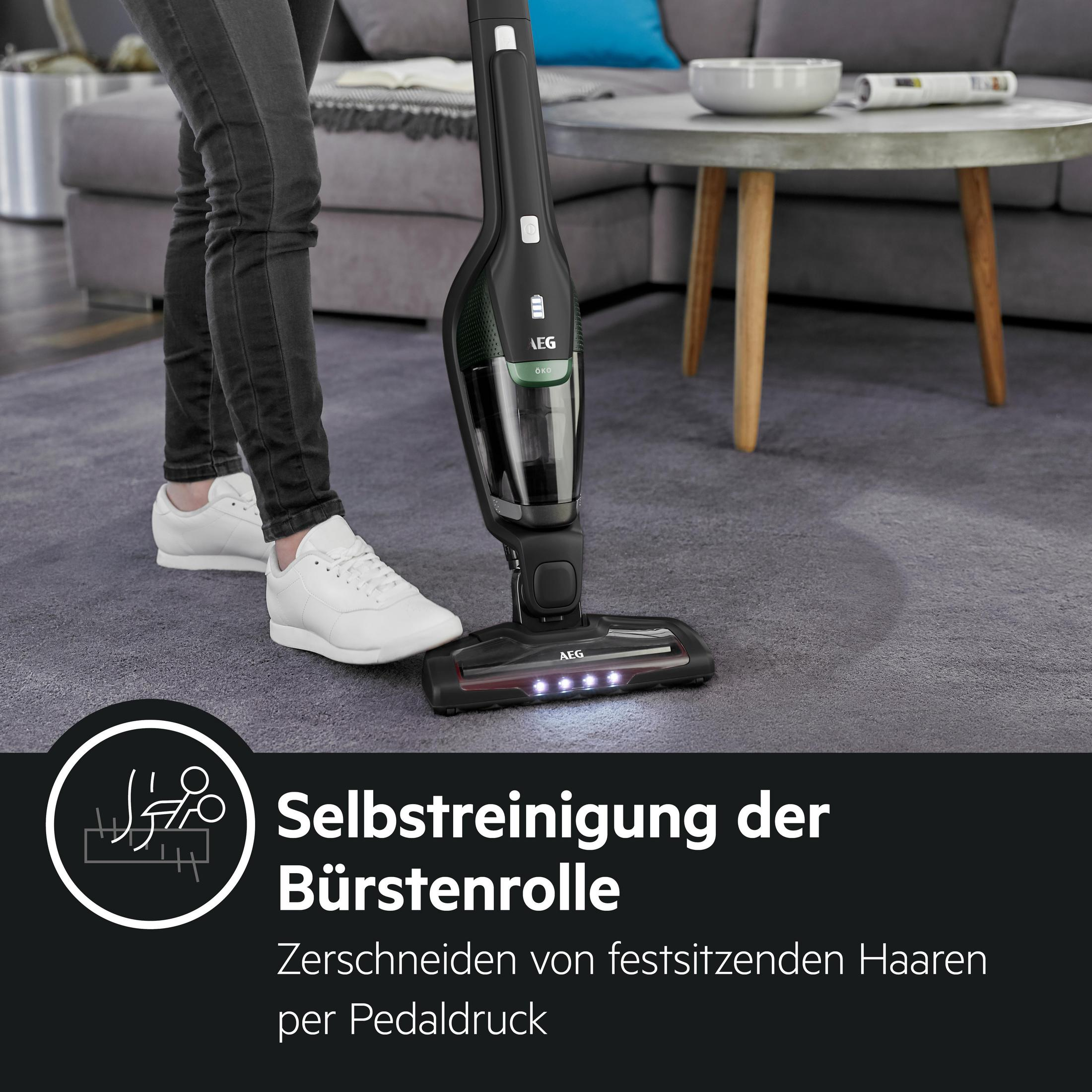 Staubsauger mit Beinen und Füßen einer Person. Der Sauger ist schwarz und hat Selbstreinigungsfunktion.