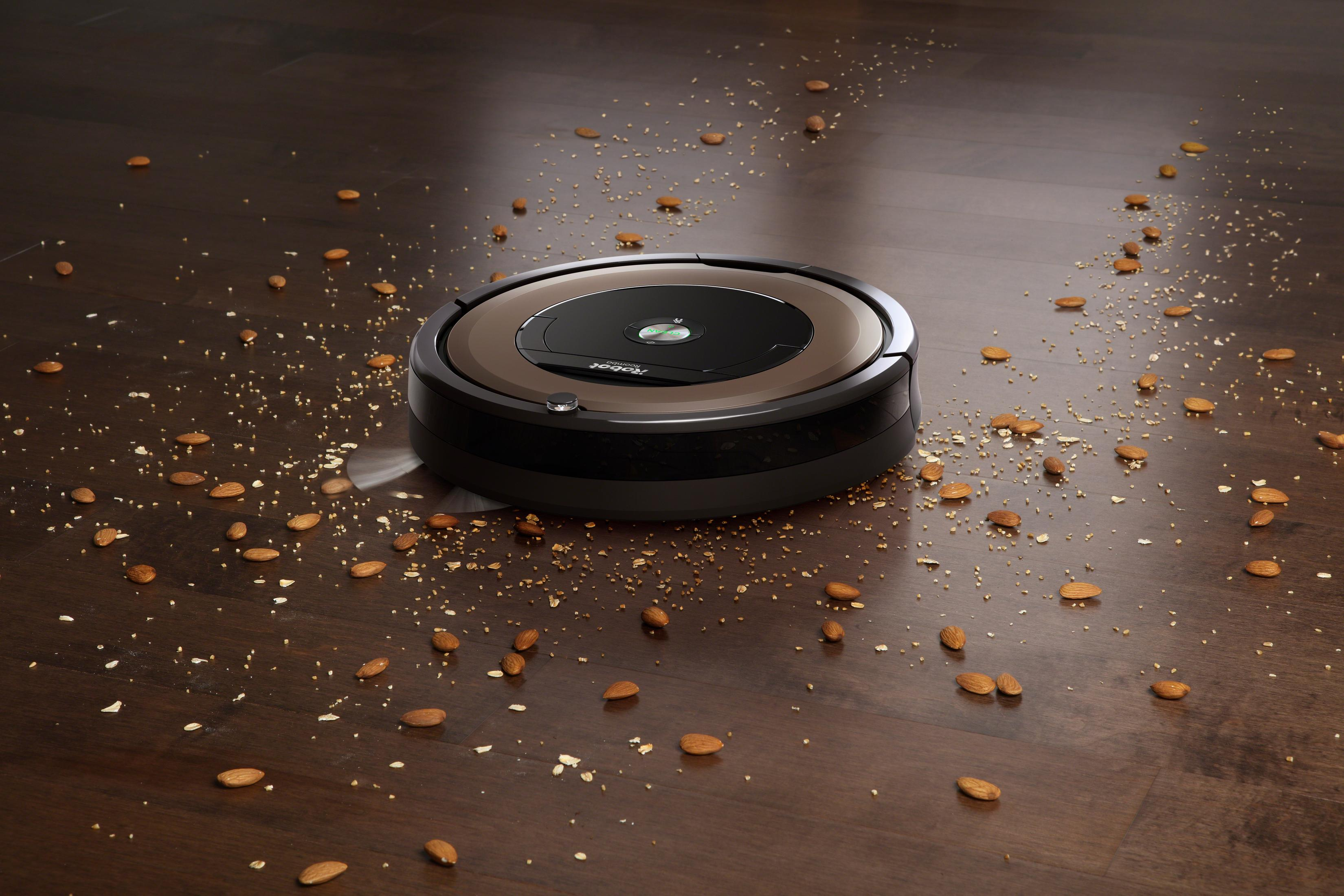 Un robot aspirapolvere su un pavimento in legno con pezzi di mandorle sparsi.