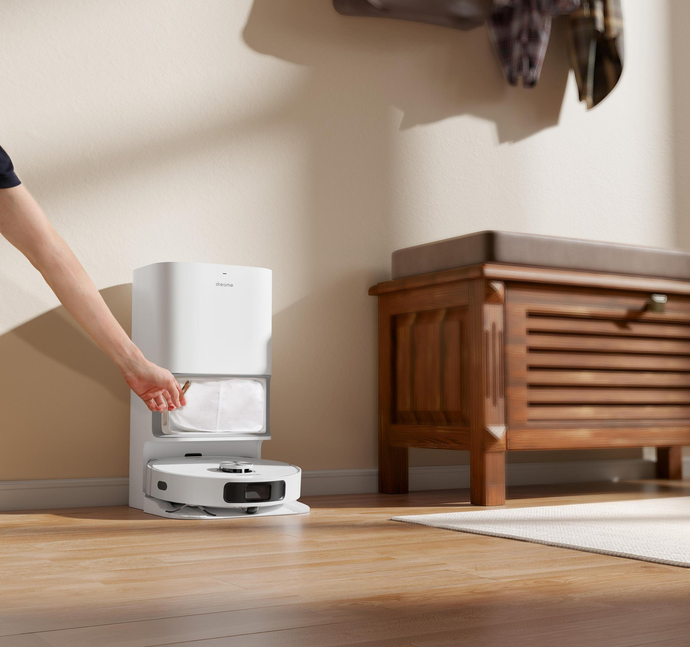 Biały odkurzacz automatyczny, z białą stacją ładującą i ręką osoby.