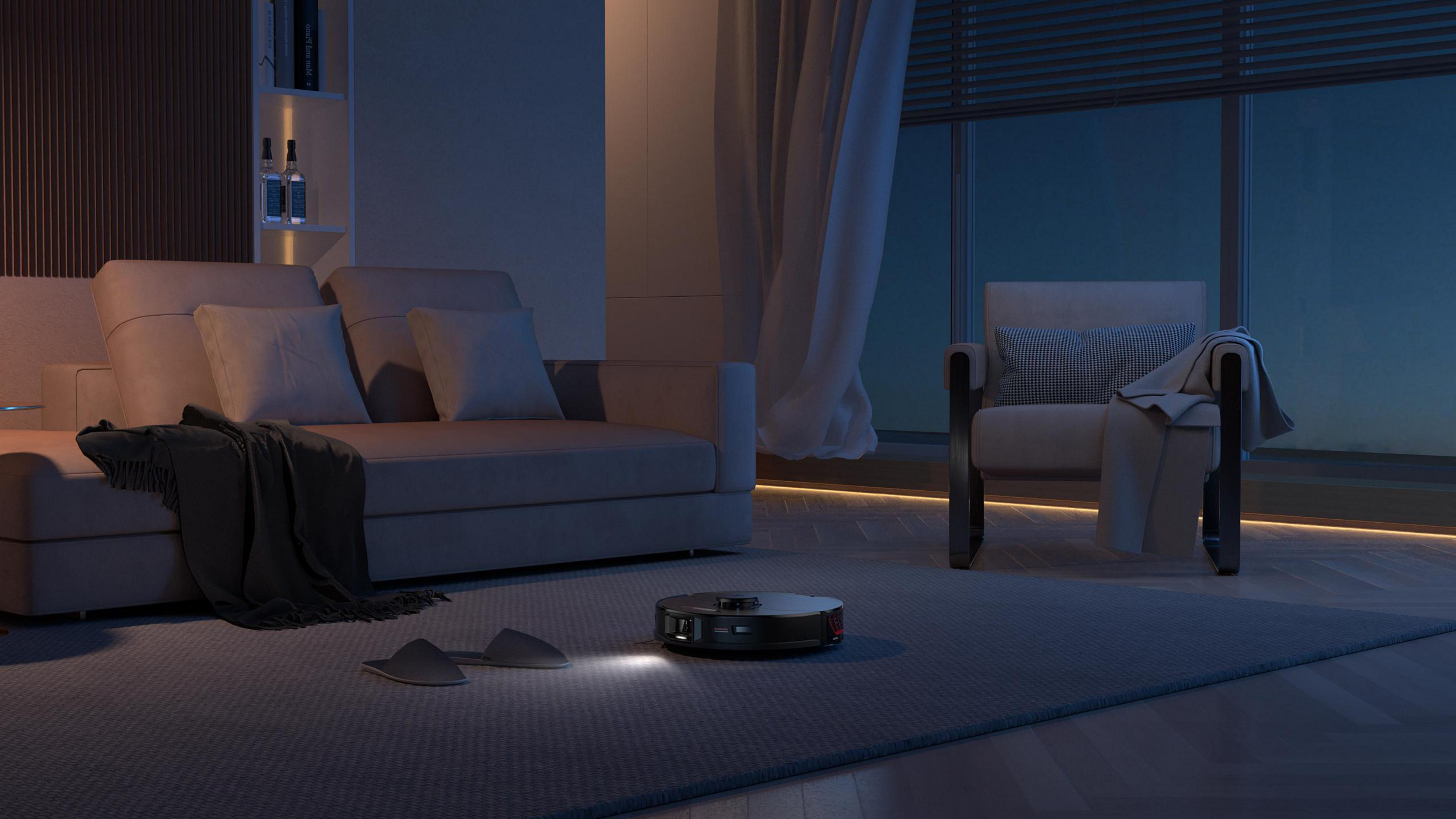 Robot sprzątający w nowoczesnym salonie. Widoczne są sofa, fotel i duże okno.