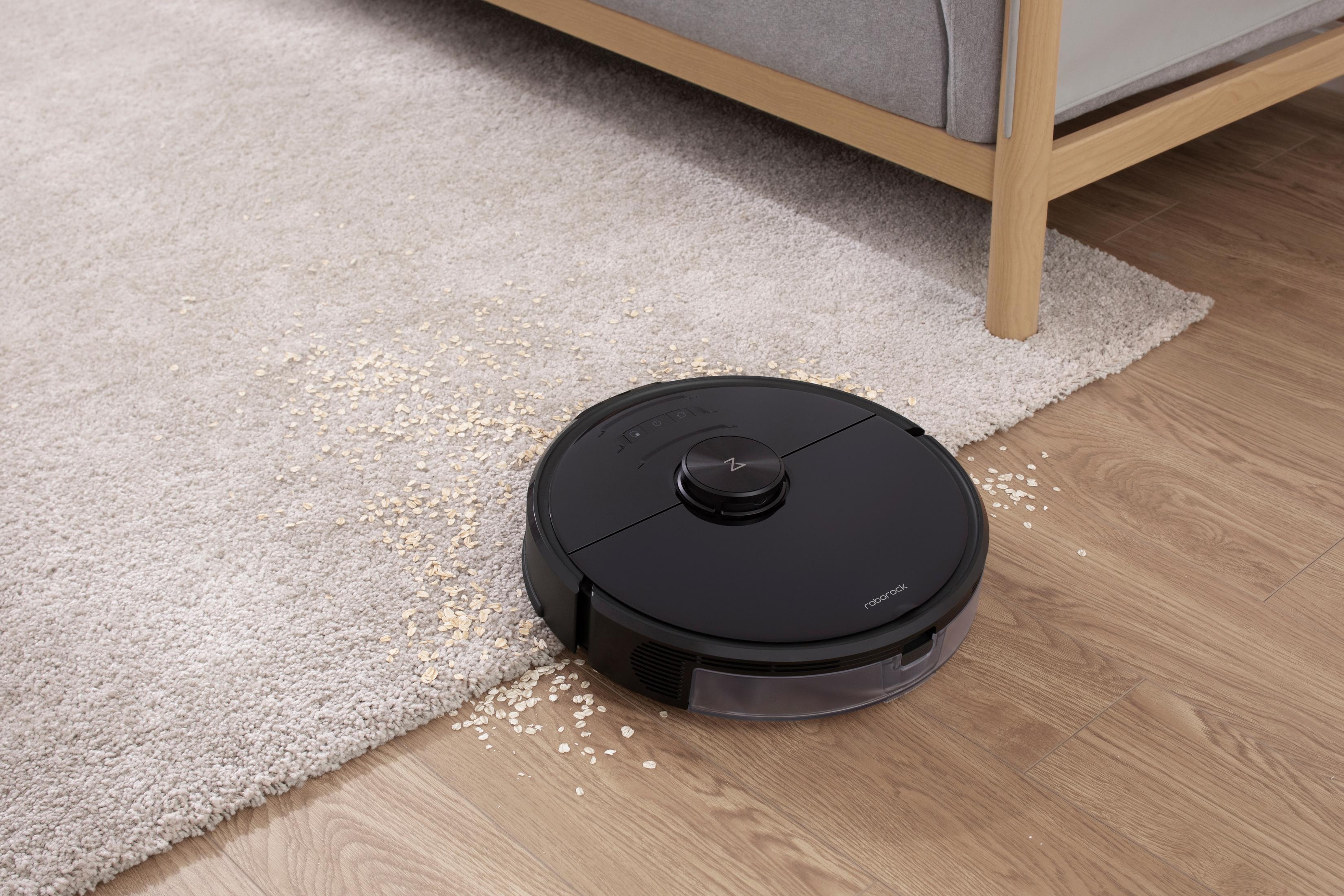 Schwarzer Roboter-Staubsauger, der einen hellen Teppich reinigt, mit verstreuten Ablagerungen.
