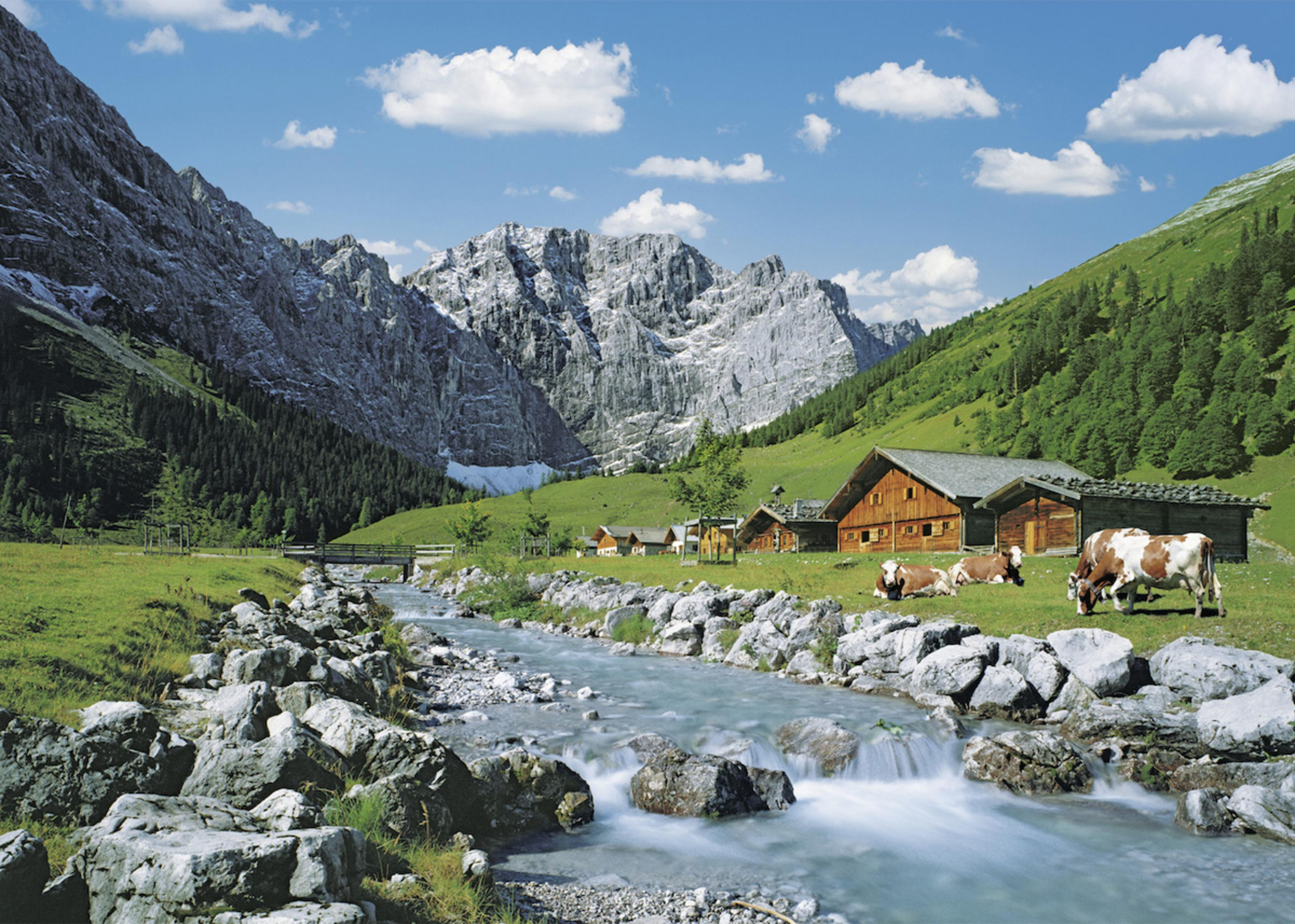 Krajobraz górski z rzeką, krowami i drewnianymi domami.
