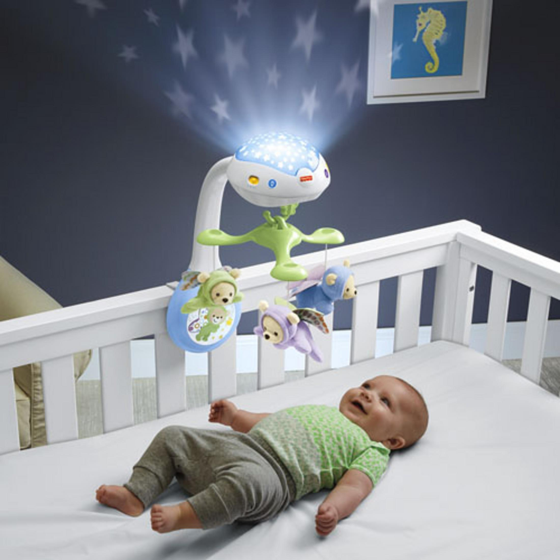 Bambino nella culla con proiettore di stelle e giocattoli appesi.