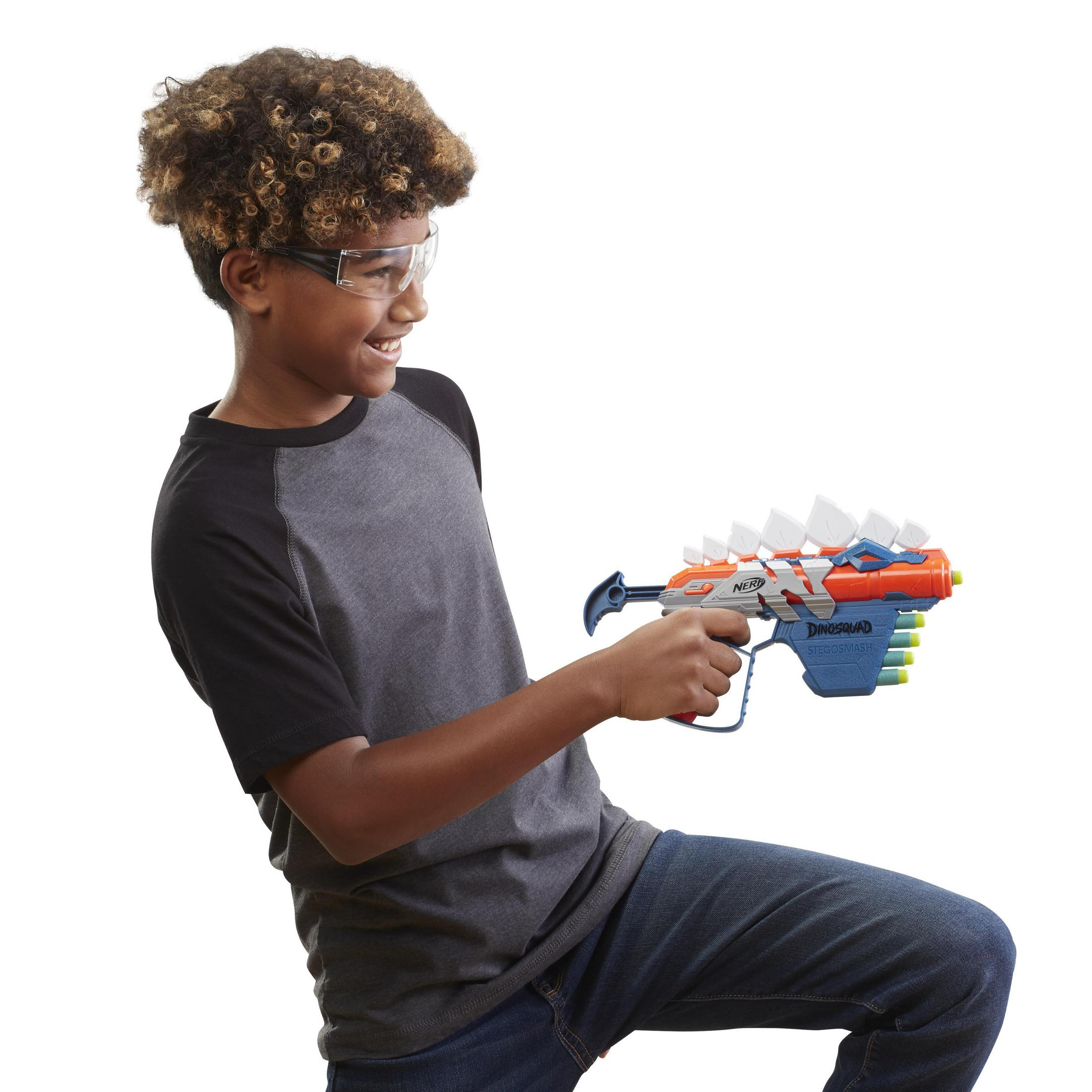 Junge hält Spielzeugpistole, trägt Brille, lächelt. Weißer Hintergrund.