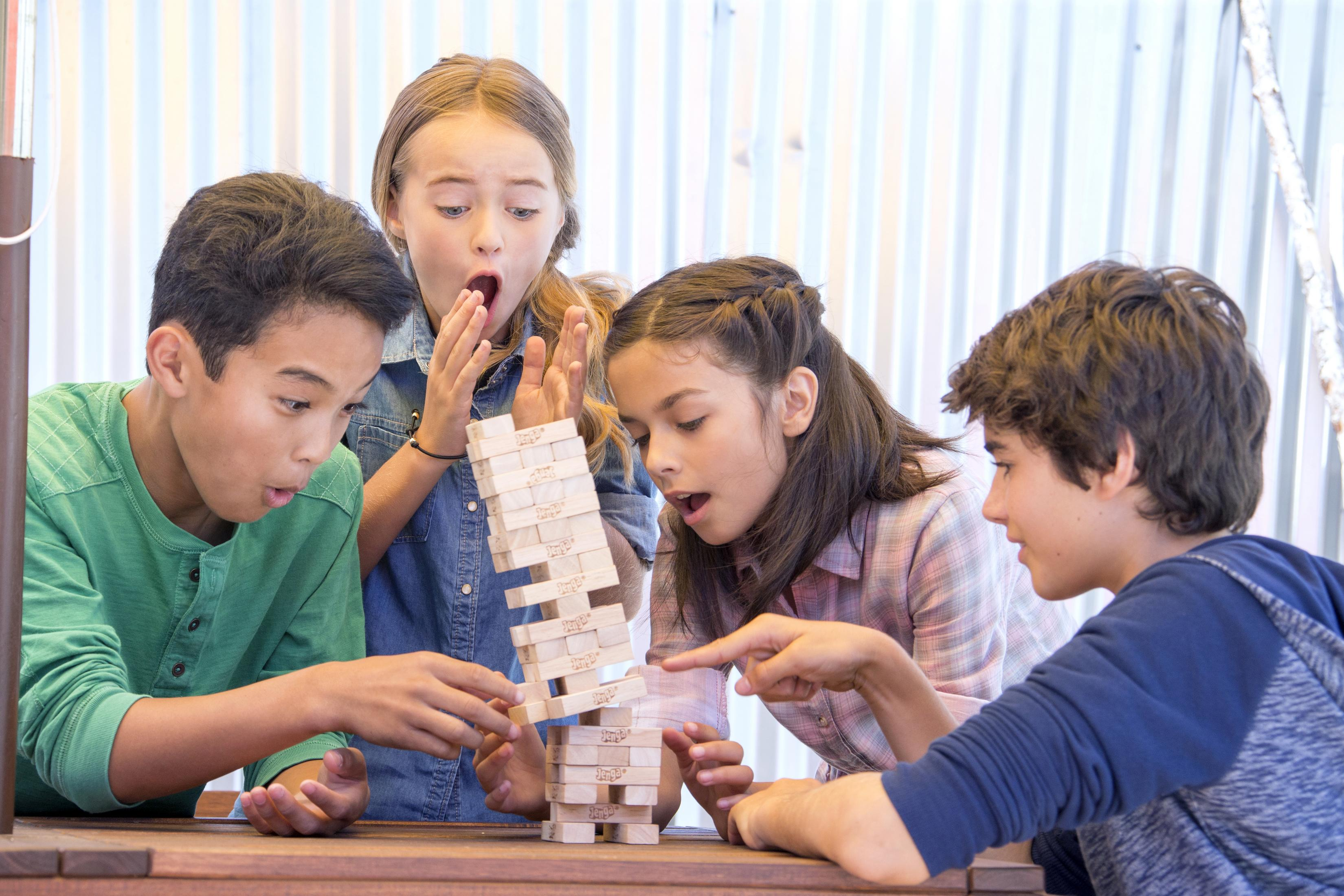 Czworo dzieci gra w Jengę, jedno wyjmuje klocek, pozostali z podziwem patrzą.