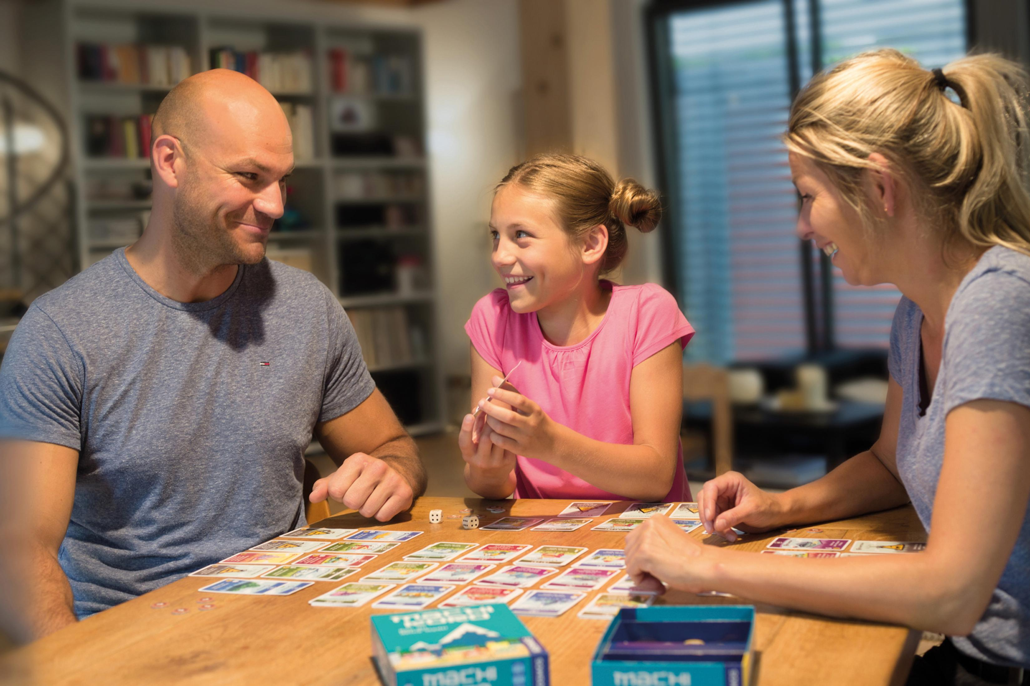 Une famille jouant à un jeu de société à une table, souriant et interagissant avec des cartes et des dés.