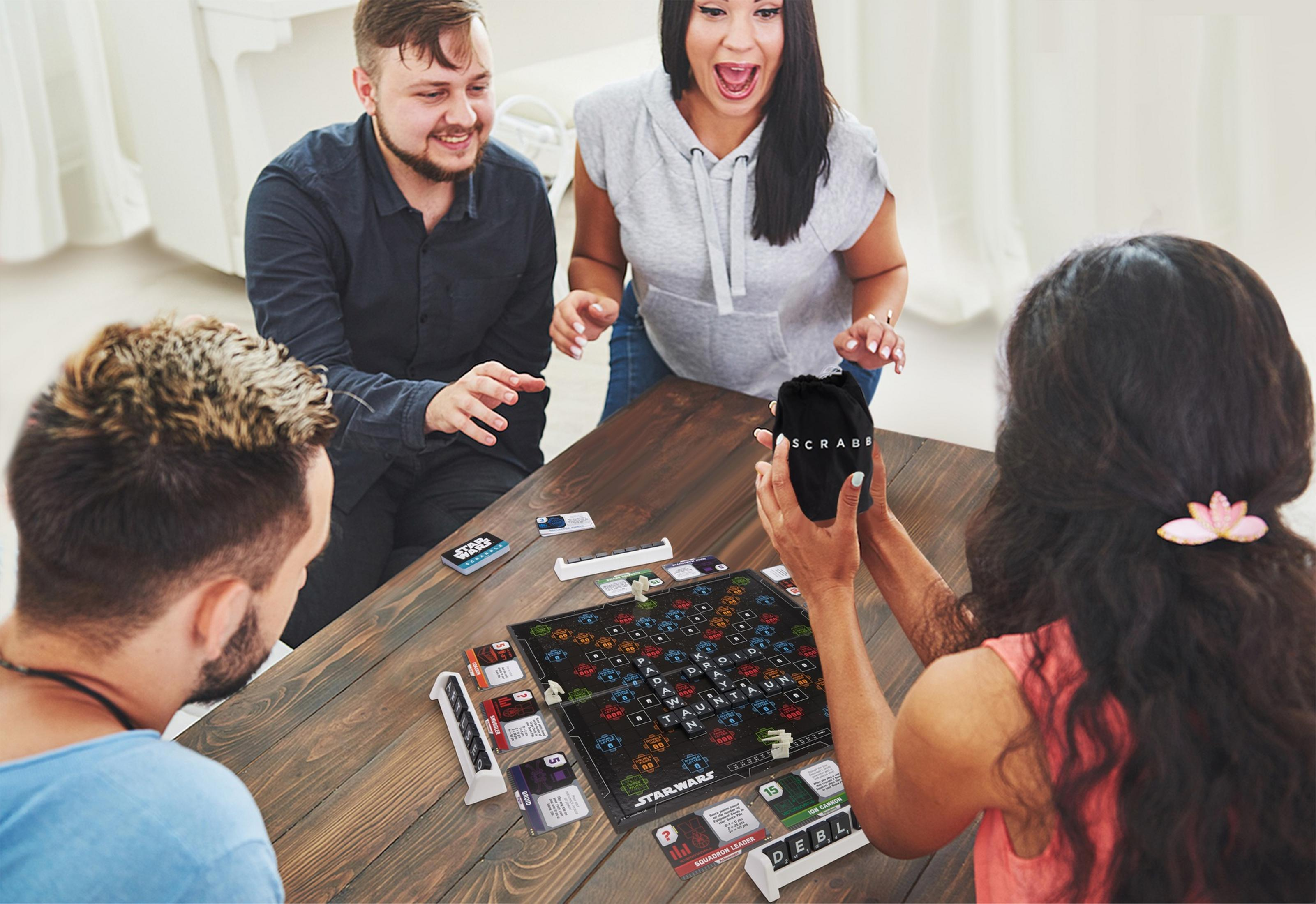 Vier Personen spielen ein Brettspiel, mit Aufregung und einem Beutel mit Spielsteinen auf dem Tisch.