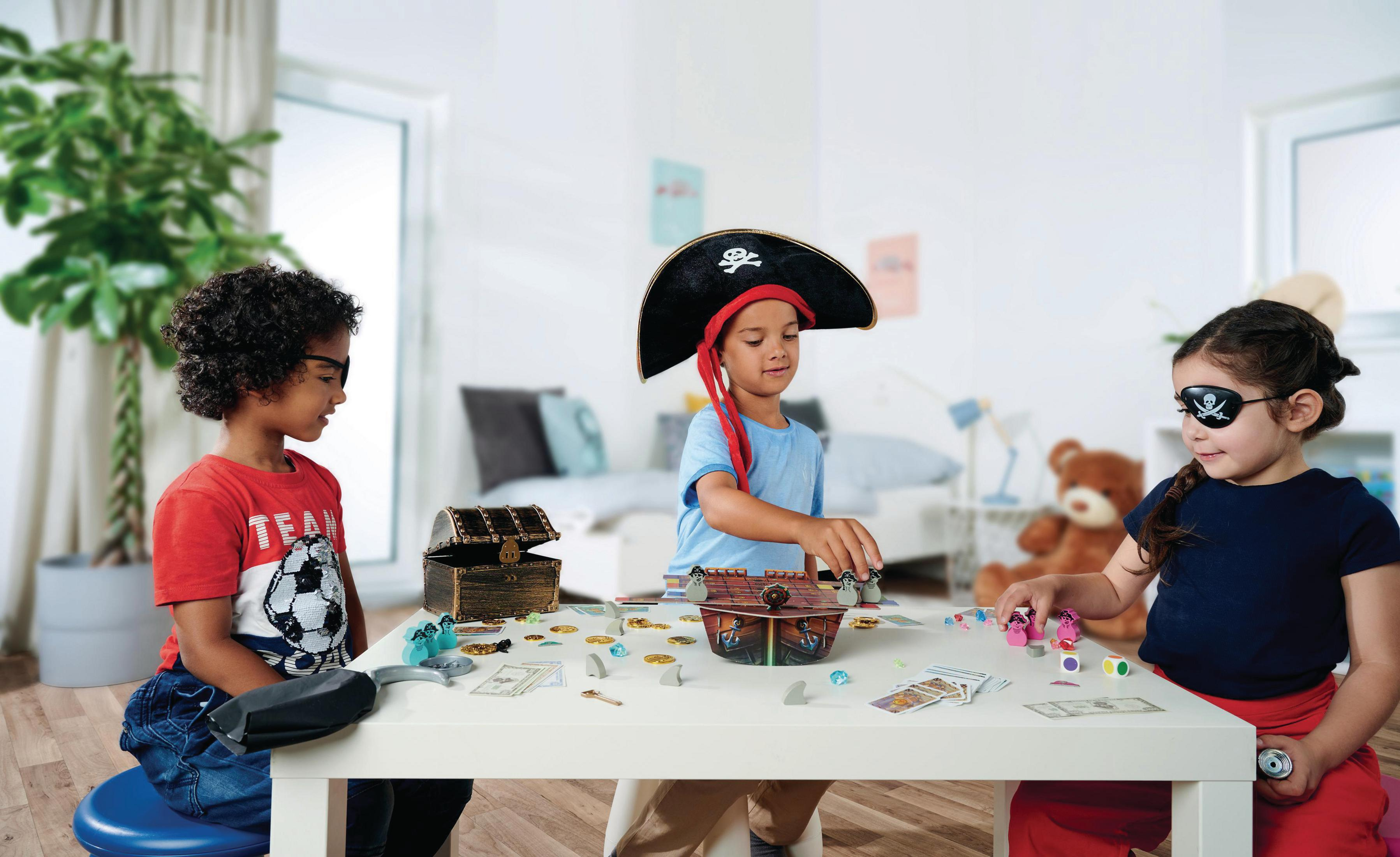 Drei Kinder spielen ein Piraten-Brettspiel auf einem weißen Tisch.