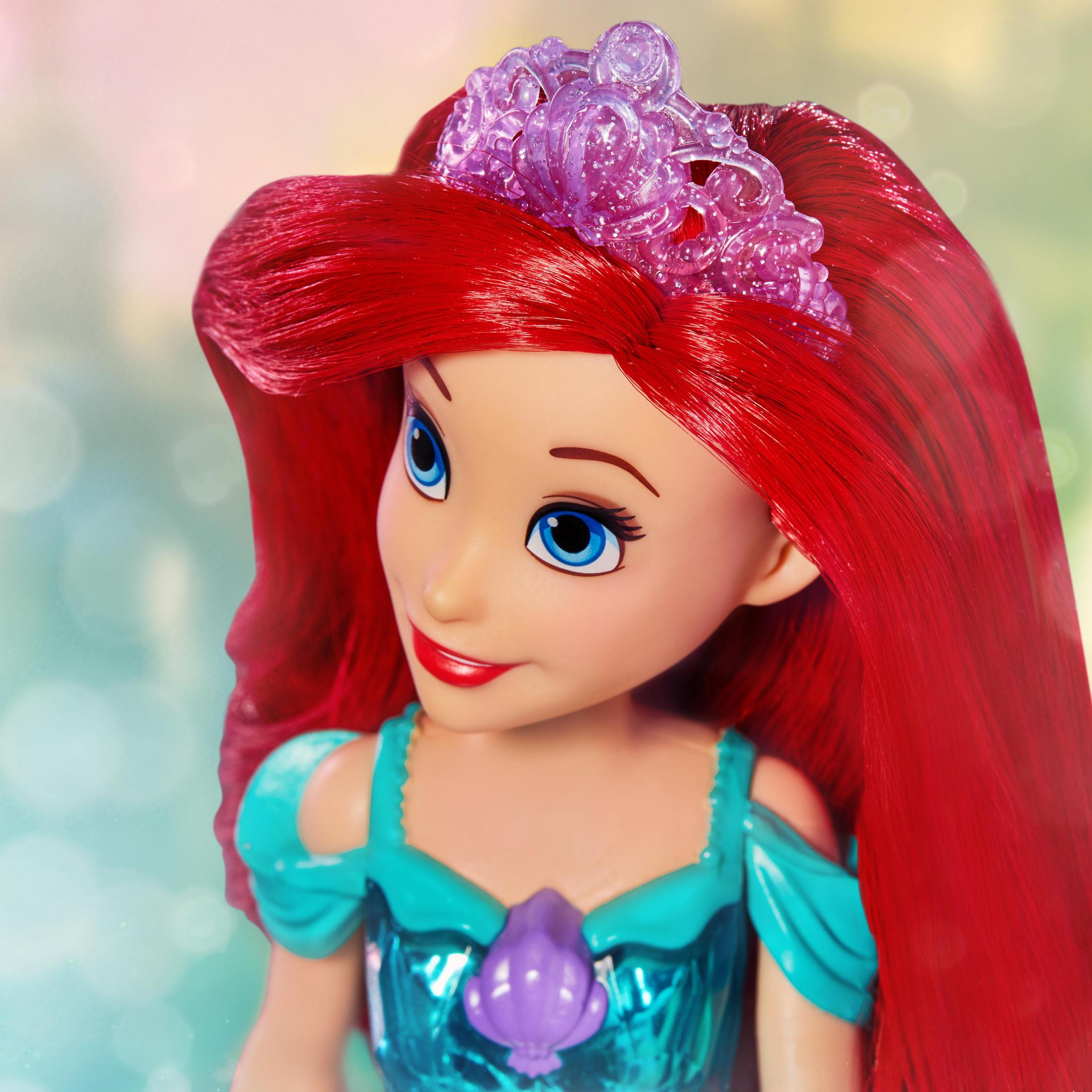 Primo piano di una bambola Ariel Disney con capelli rossi e tiara viola, sorridente, su sfondo sfocato.