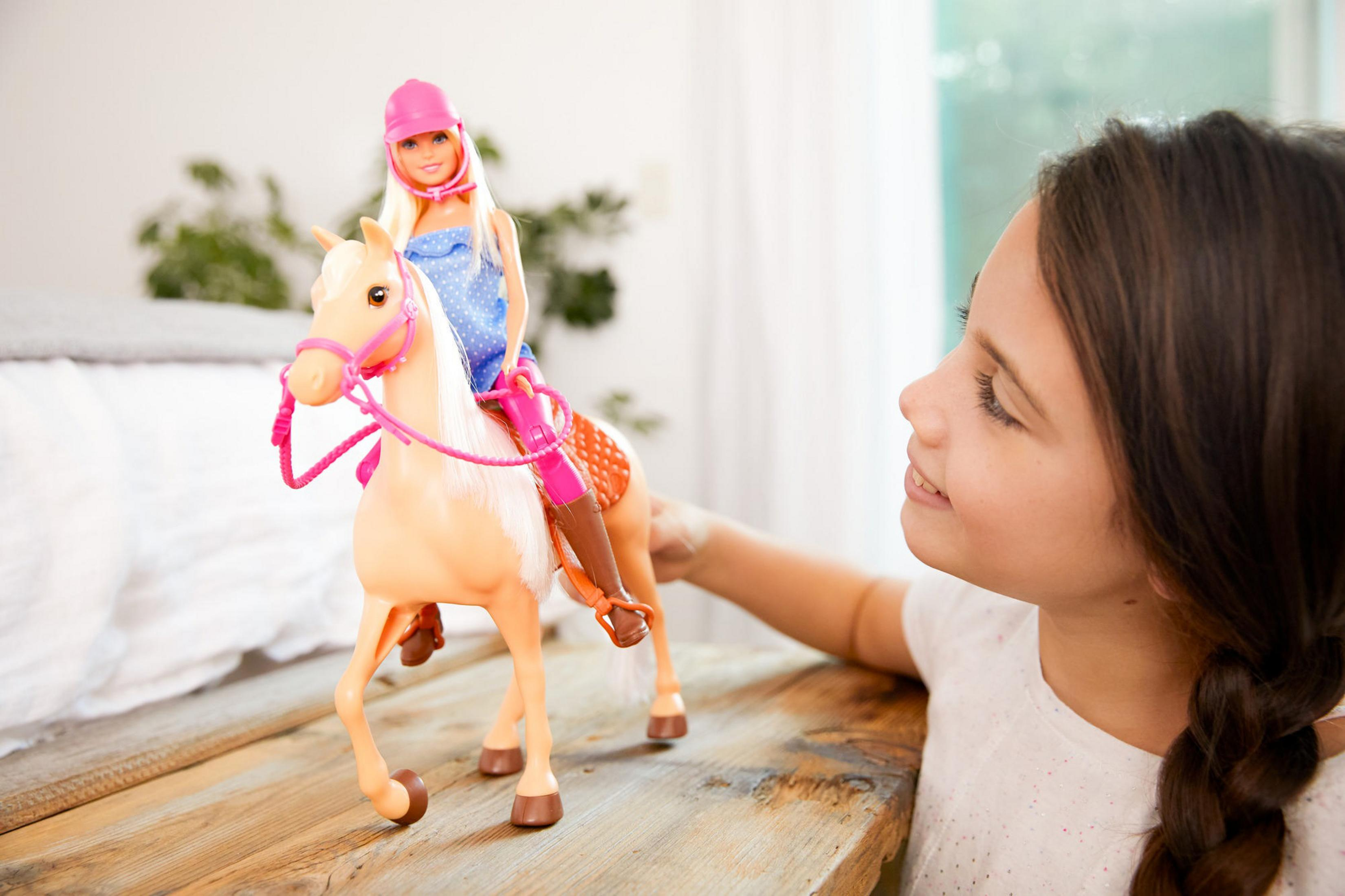 Ein junges Mädchen spielt mit einer Barbie-Puppe, die auf einem Spielzeugpferd auf einer Holzoberfläche reitet.