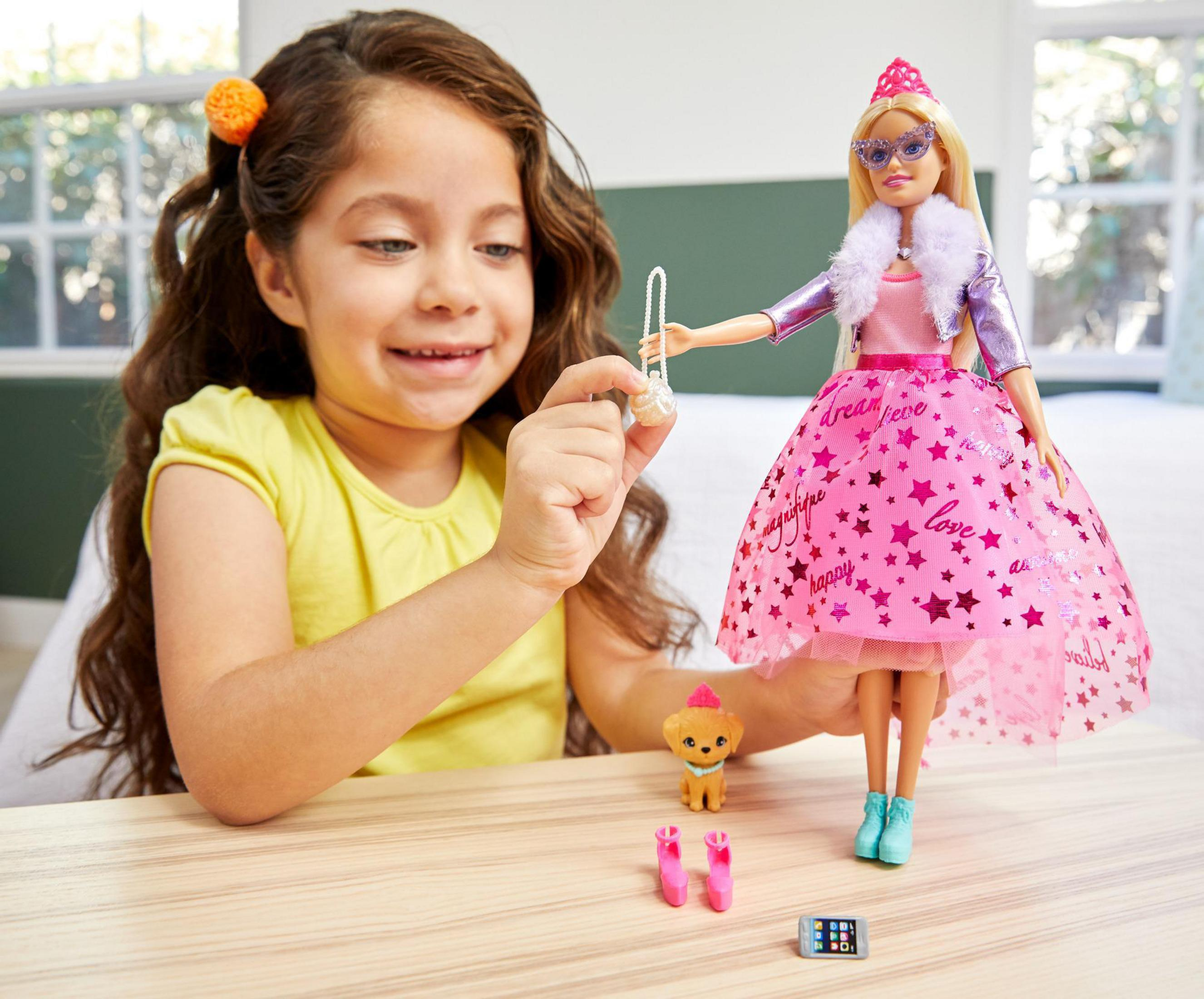 Ein Mädchen spielt mit einer Barbie-Puppe, einem Hund und Zubehör. Die Puppe ist rosa und trägt eine Sonnenbrille.