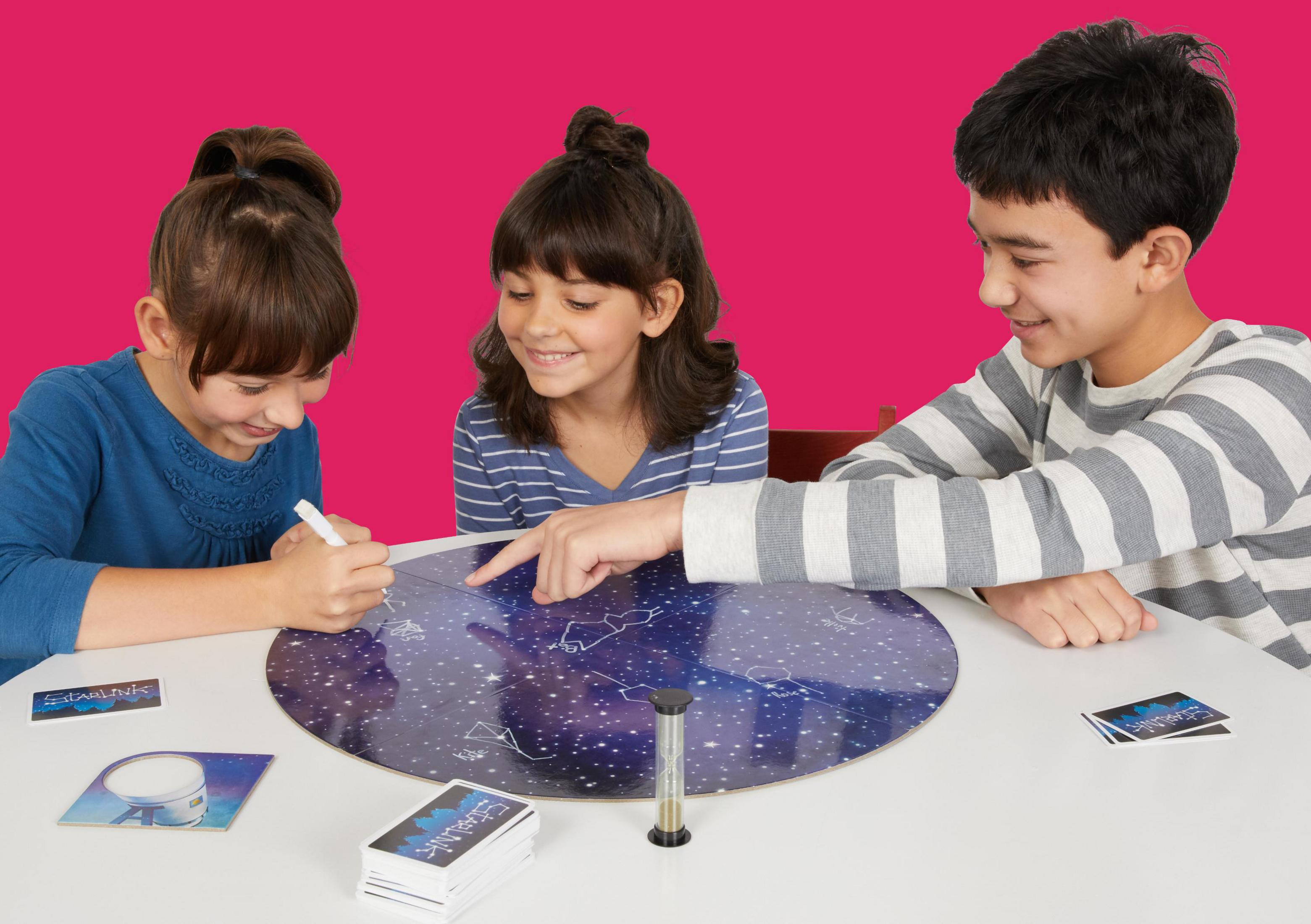 Drei Kinder spielen ein Brettspiel auf einem Tisch. Es gibt ein Spielbrett, Karten und einen Timer.