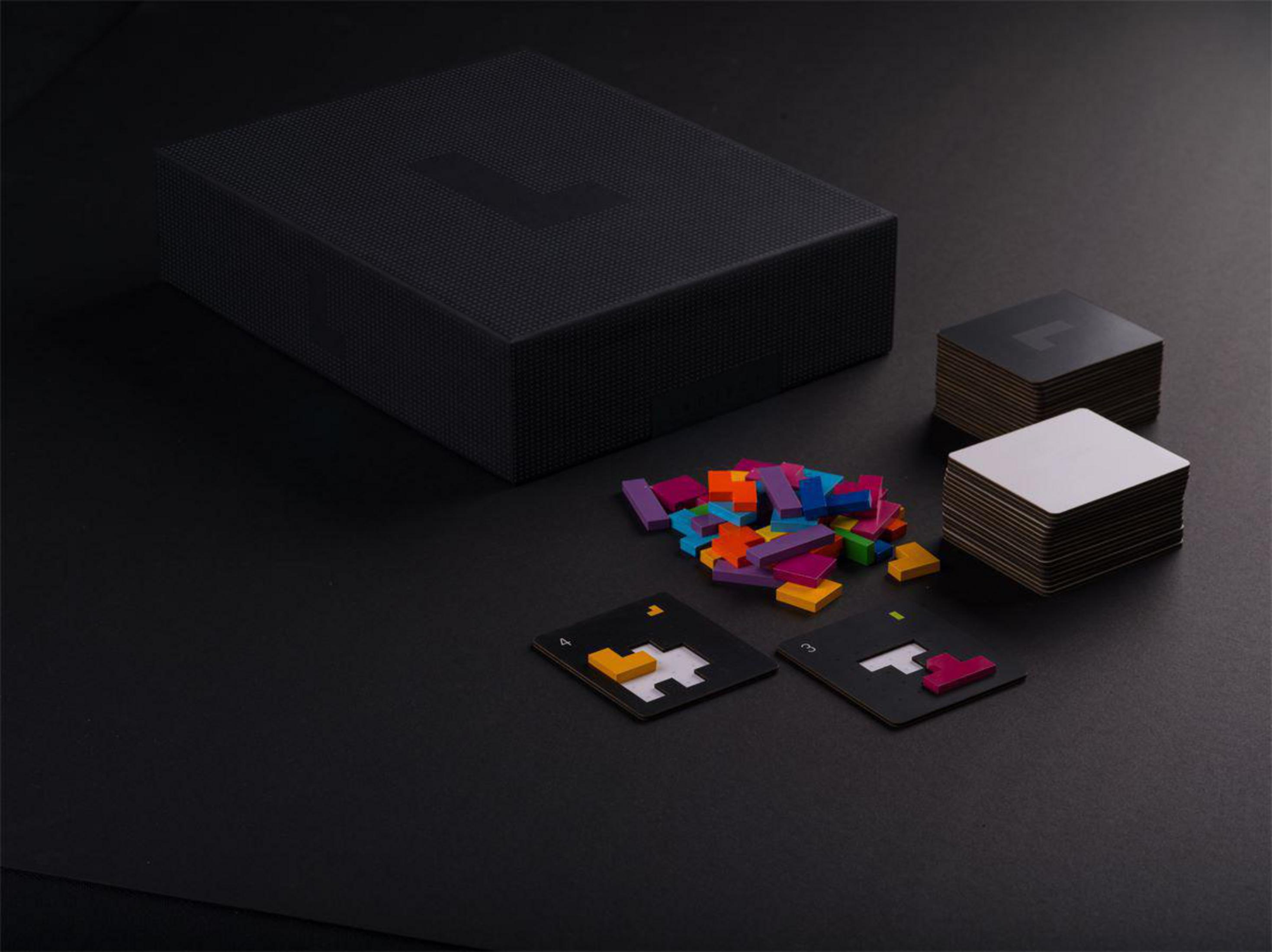 Schwarze Box mit farbigen Formen, Karten und Holzstücken auf schwarzem Untergrund. Schatten erzeugen Tiefe.