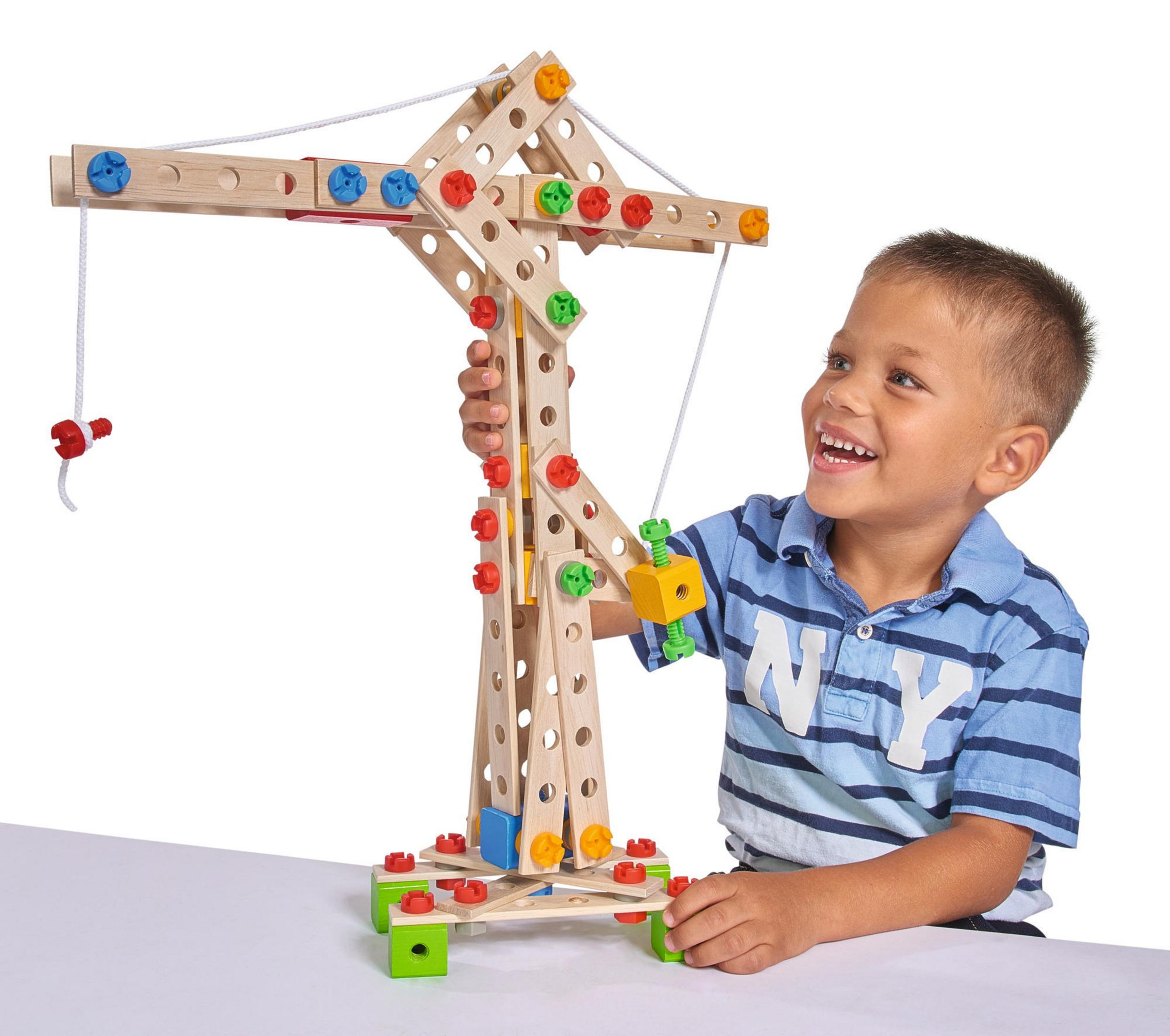 Ein Kind lächelt, während es mit einem hölzernen Spielzeugkran spielt, der mit bunten Kunststoffschrauben und einem Seilzugsystem ausgestattet ist.
