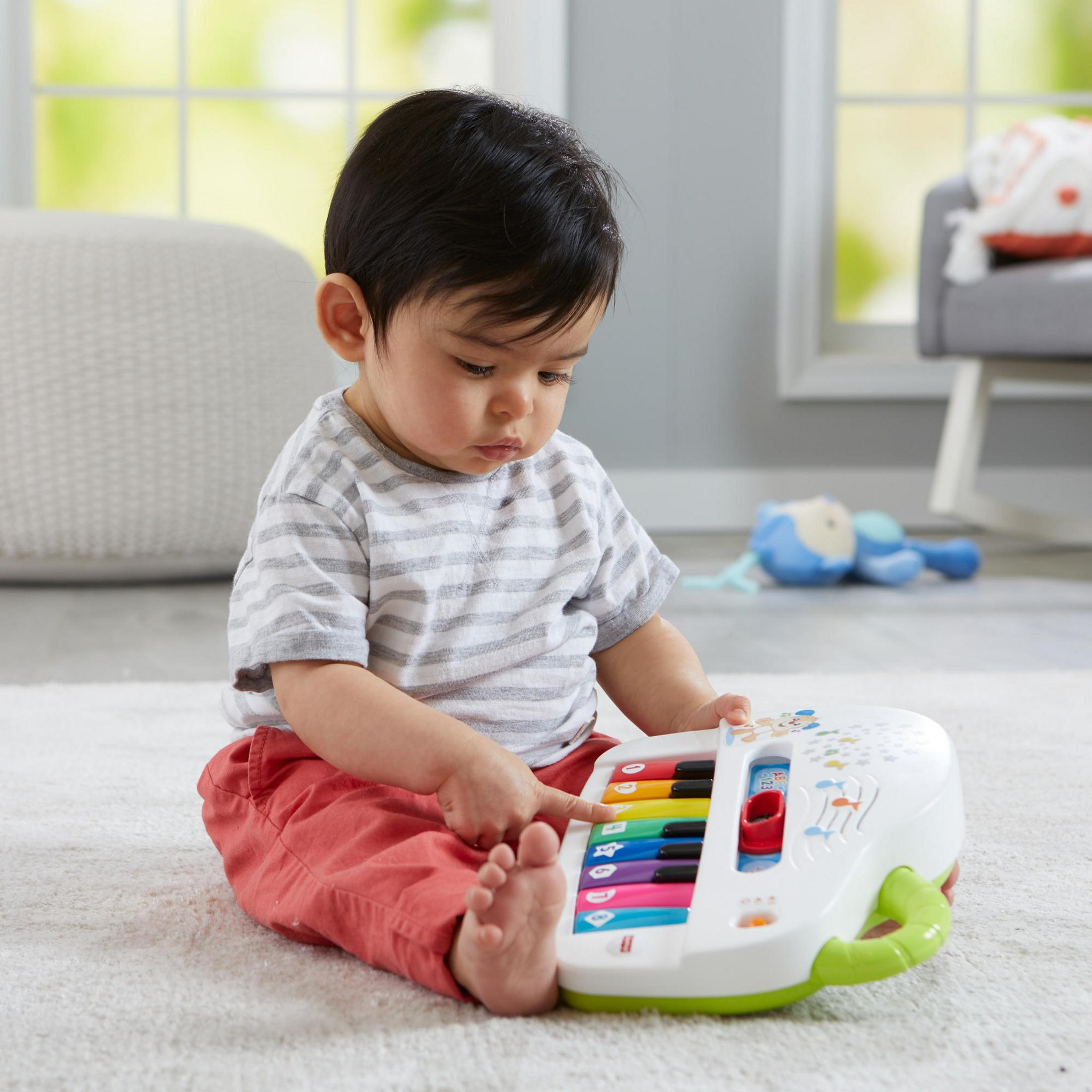 Baby spielt Spielzeug-Klavier. Kind sitzt auf einem Teppich und interagiert mit einem bunten Klavierspielzeug.