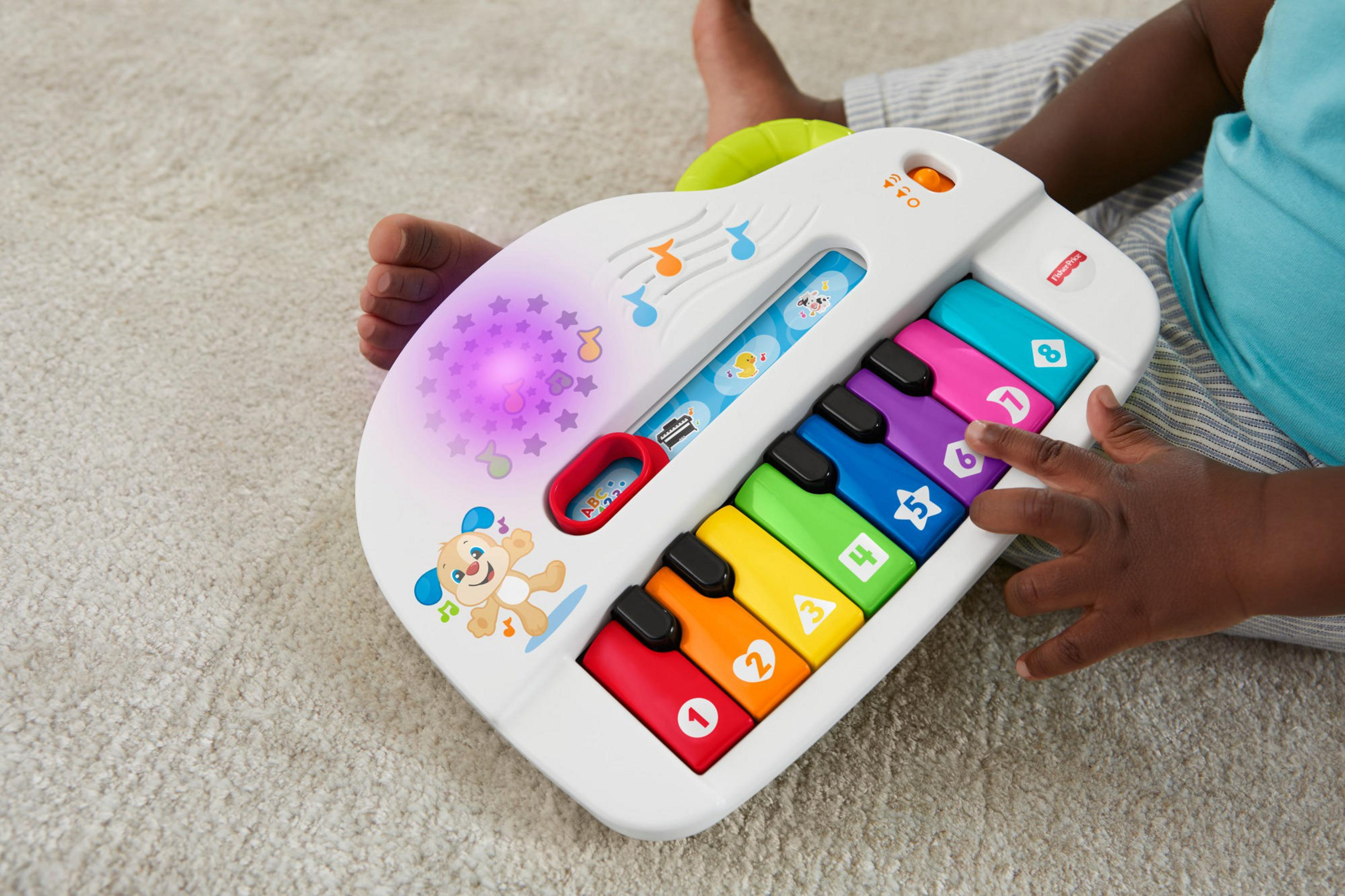Ein Baby spielt mit einem Spielzeugklavier in Gitarrenform.