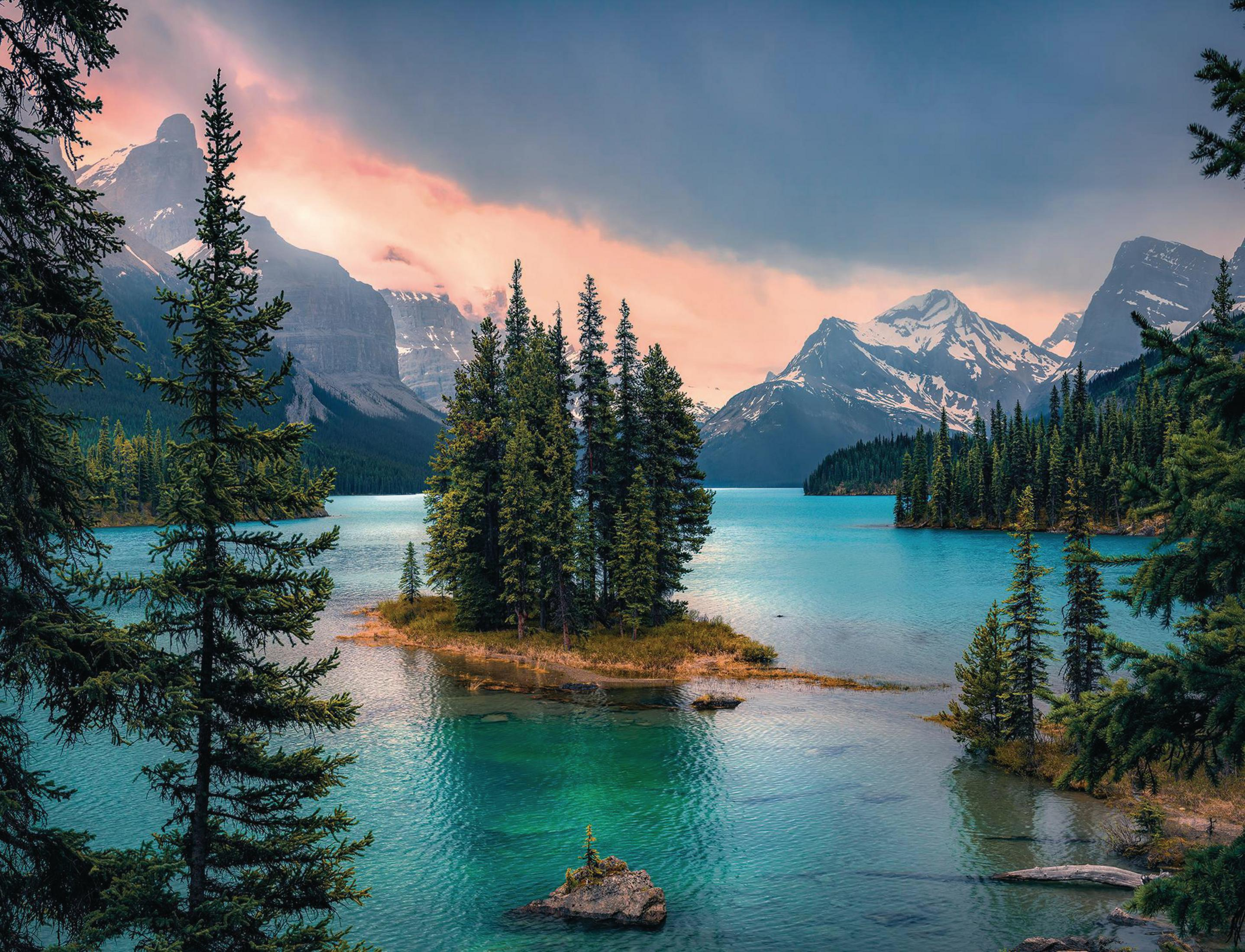 Paesaggio con lago, isola con alberi, montagne e cielo colorato al tramonto.